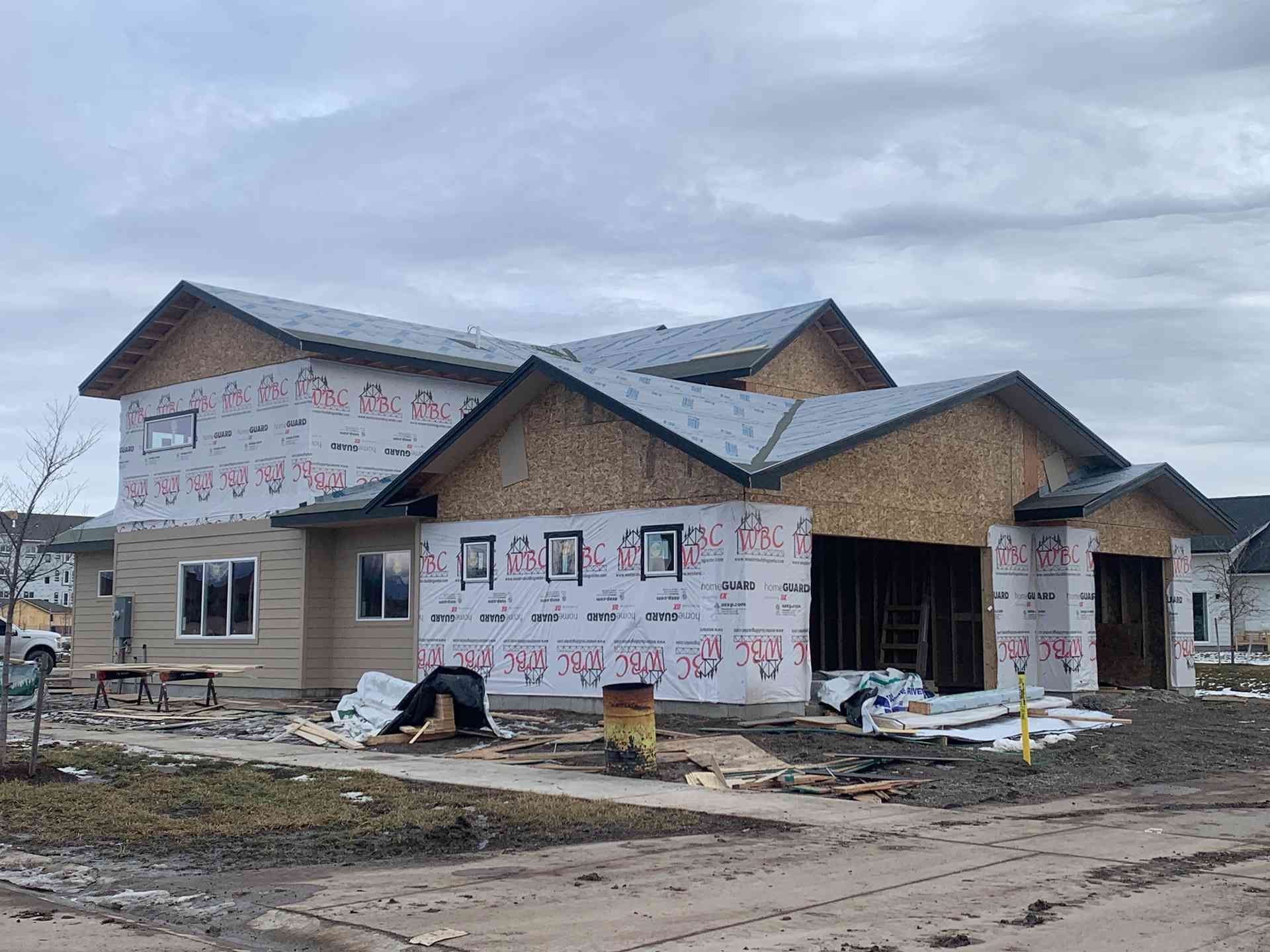 Partially built house under construction with wrapped exterior and workers’ materials on a muddy site