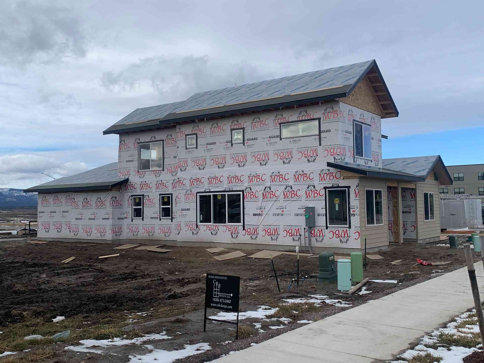 Partially built two-story house with pink wrap and solar panels beside a sidewalk under cloudy skies