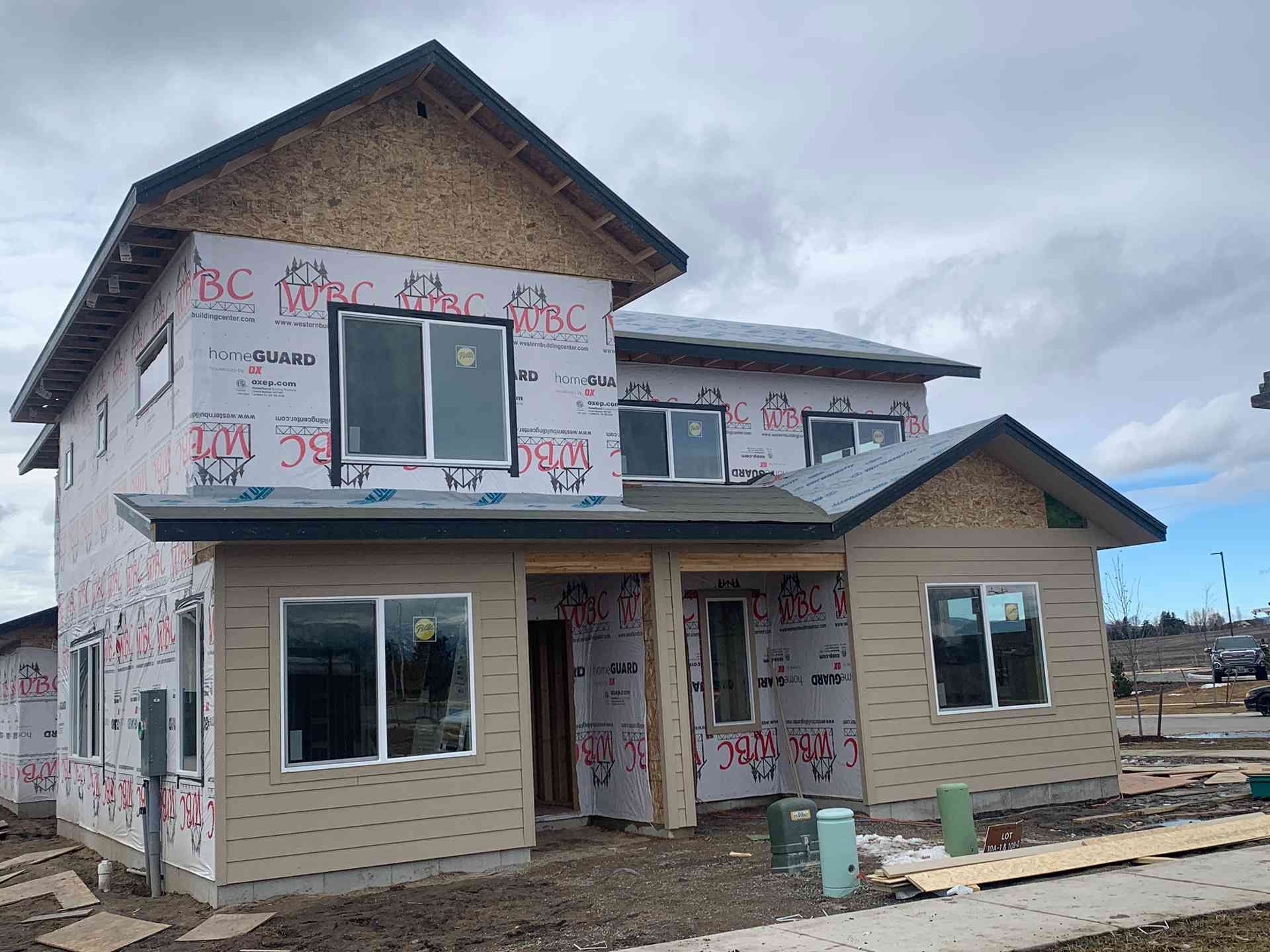 Partially built two-story house with white wrap, beige siding, and overcast sky