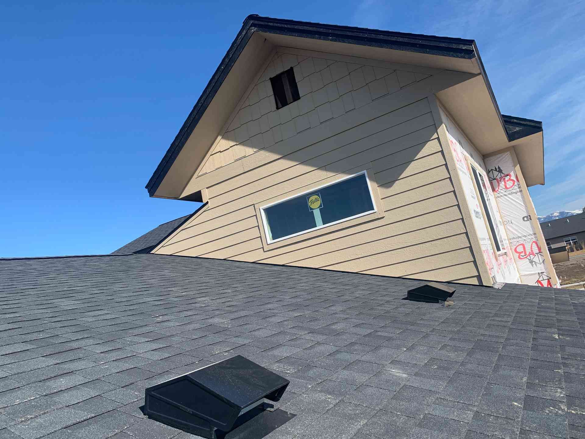House roof with a skylight and beige siding under a blue sky.