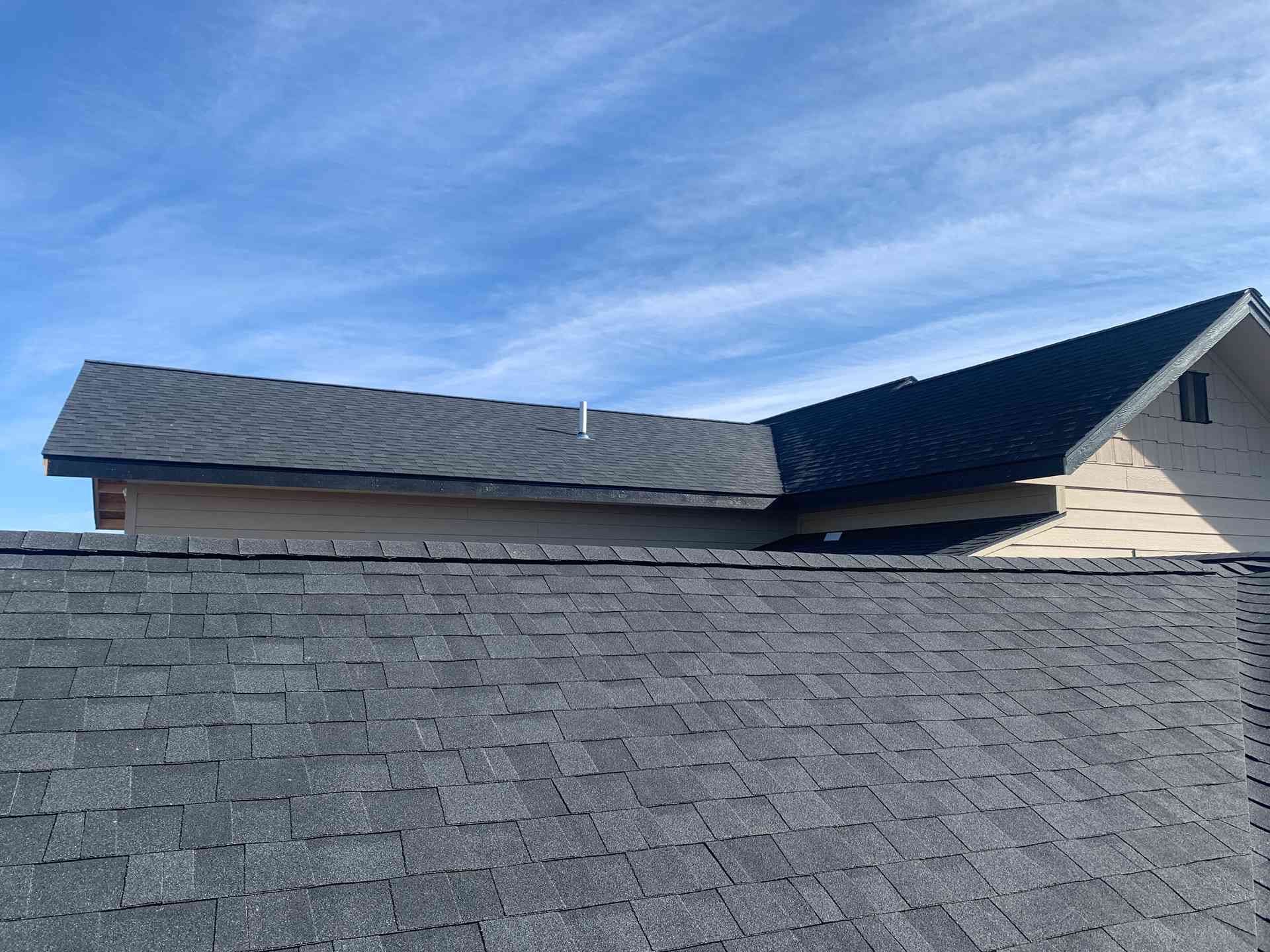 Roofline with gray shingles and dormer under a blue sky