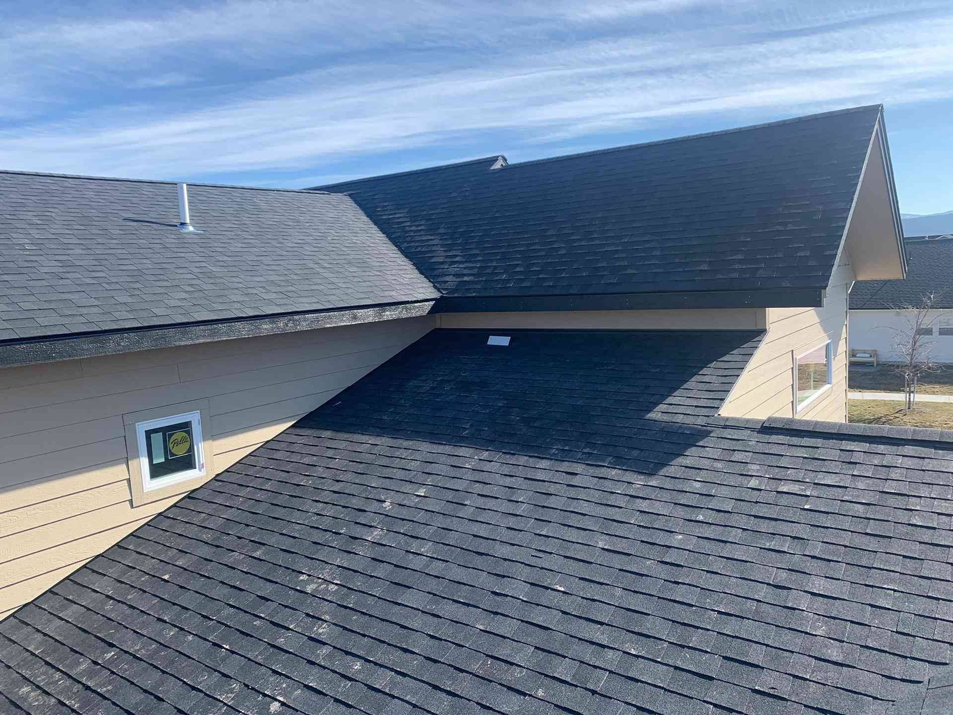 Dark shingled roof with multiple sloped sections and blue sky above