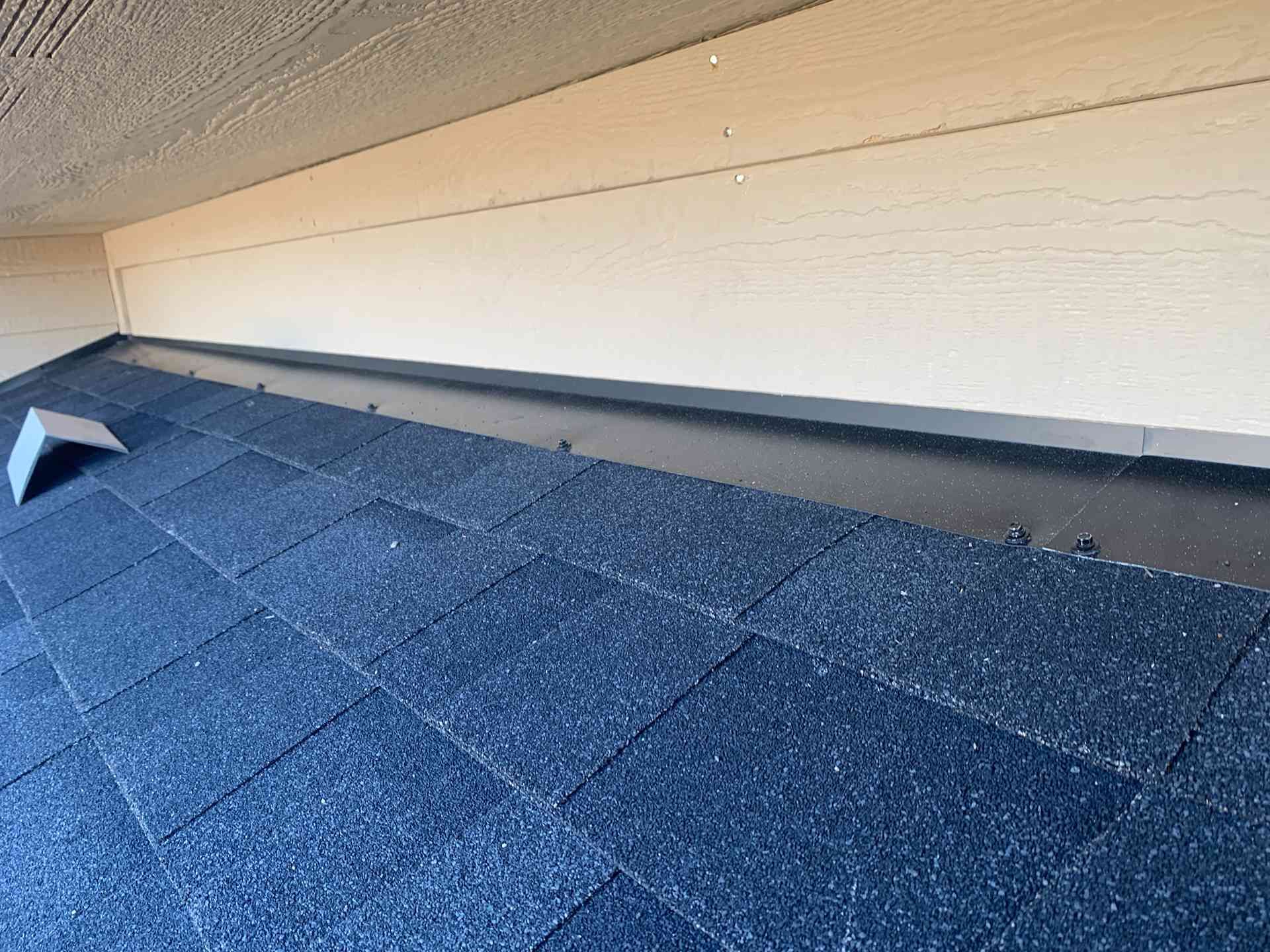 Blue shingle roof under a beige eave with a small vent near the left side