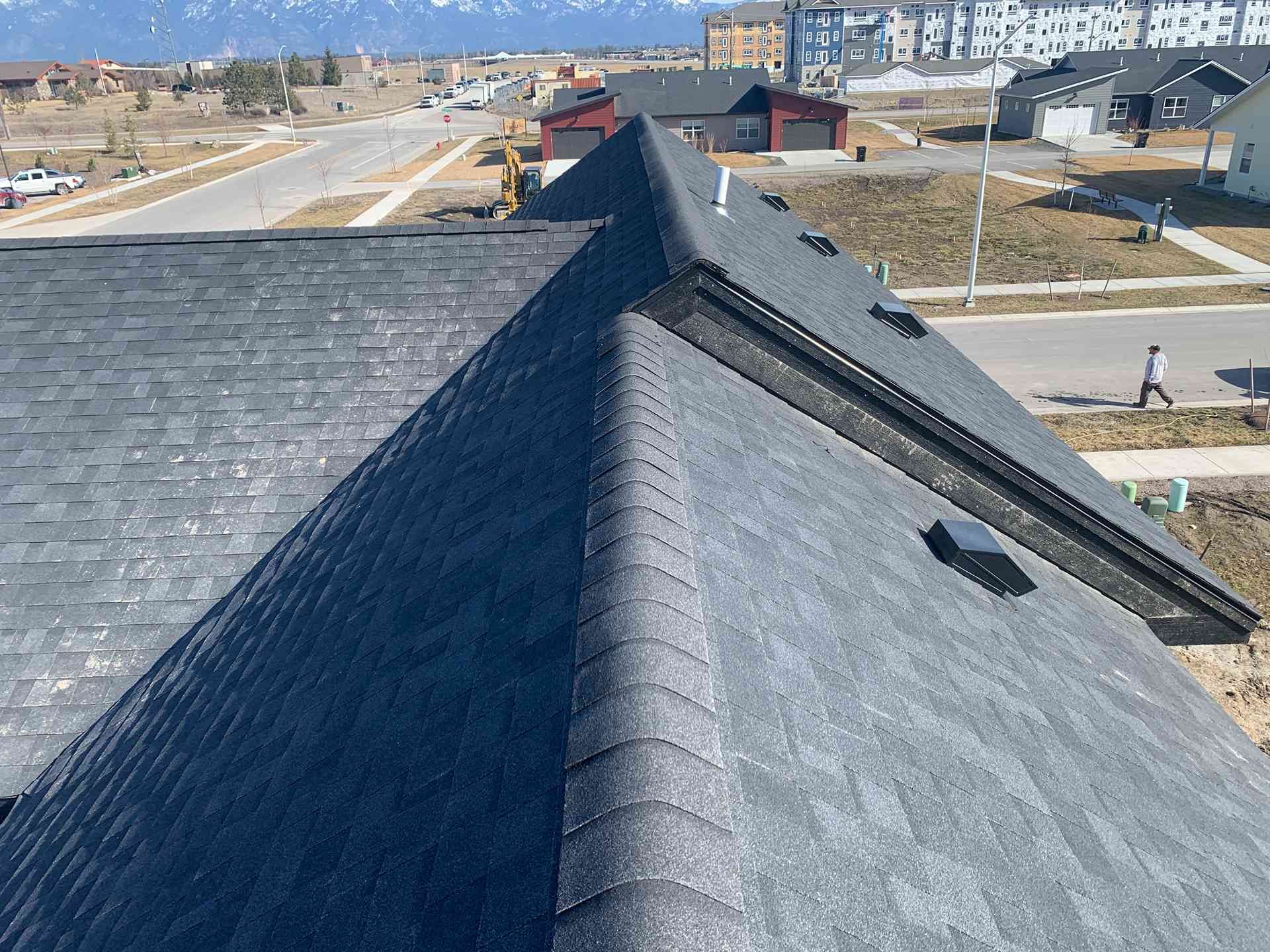 Rooftop with gray shingles overlooking a suburban neighborhood on a clear day