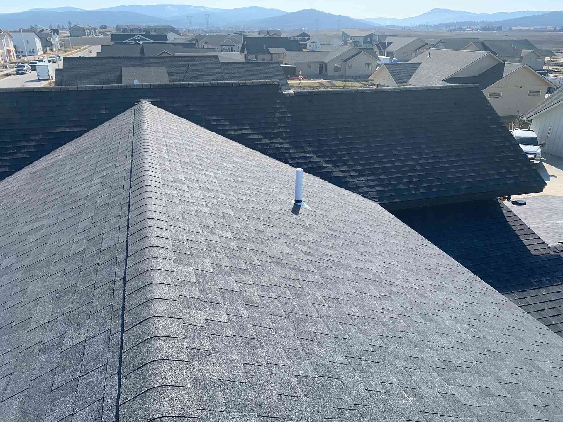 Rooftops with dark shingles under a clear sky, viewed from above with distant mountains in the background
