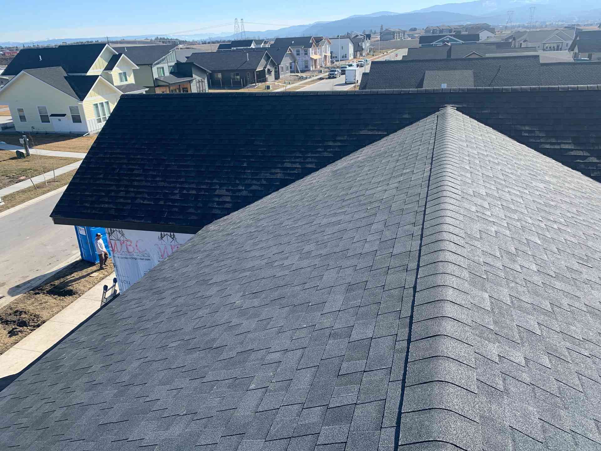 Gray shingled roof ridge on a new house in a suburban neighborhood under clear daylight