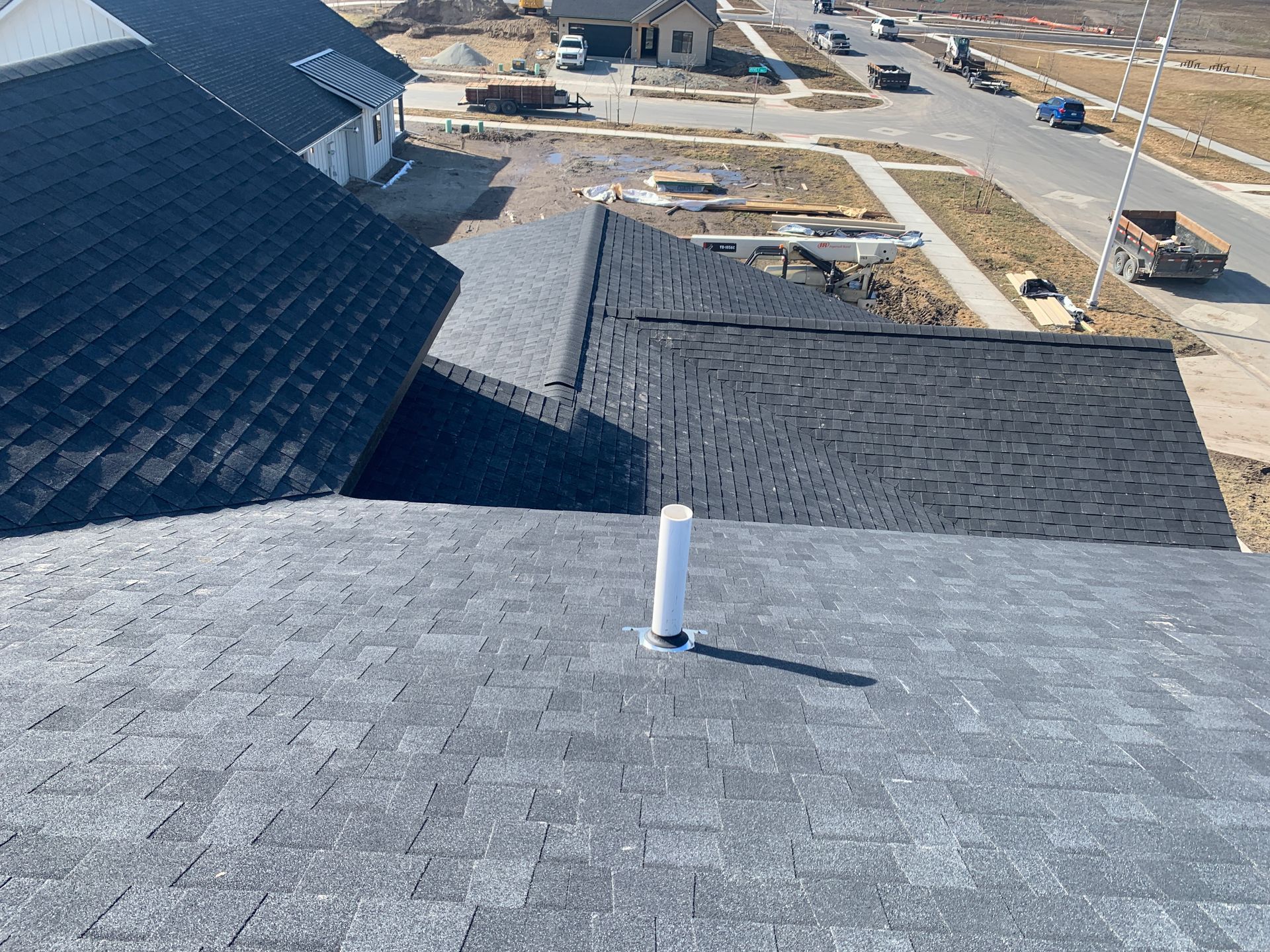 Rooftops of a suburban neighborhood with gray shingles and a white vent pipe in the foreground.