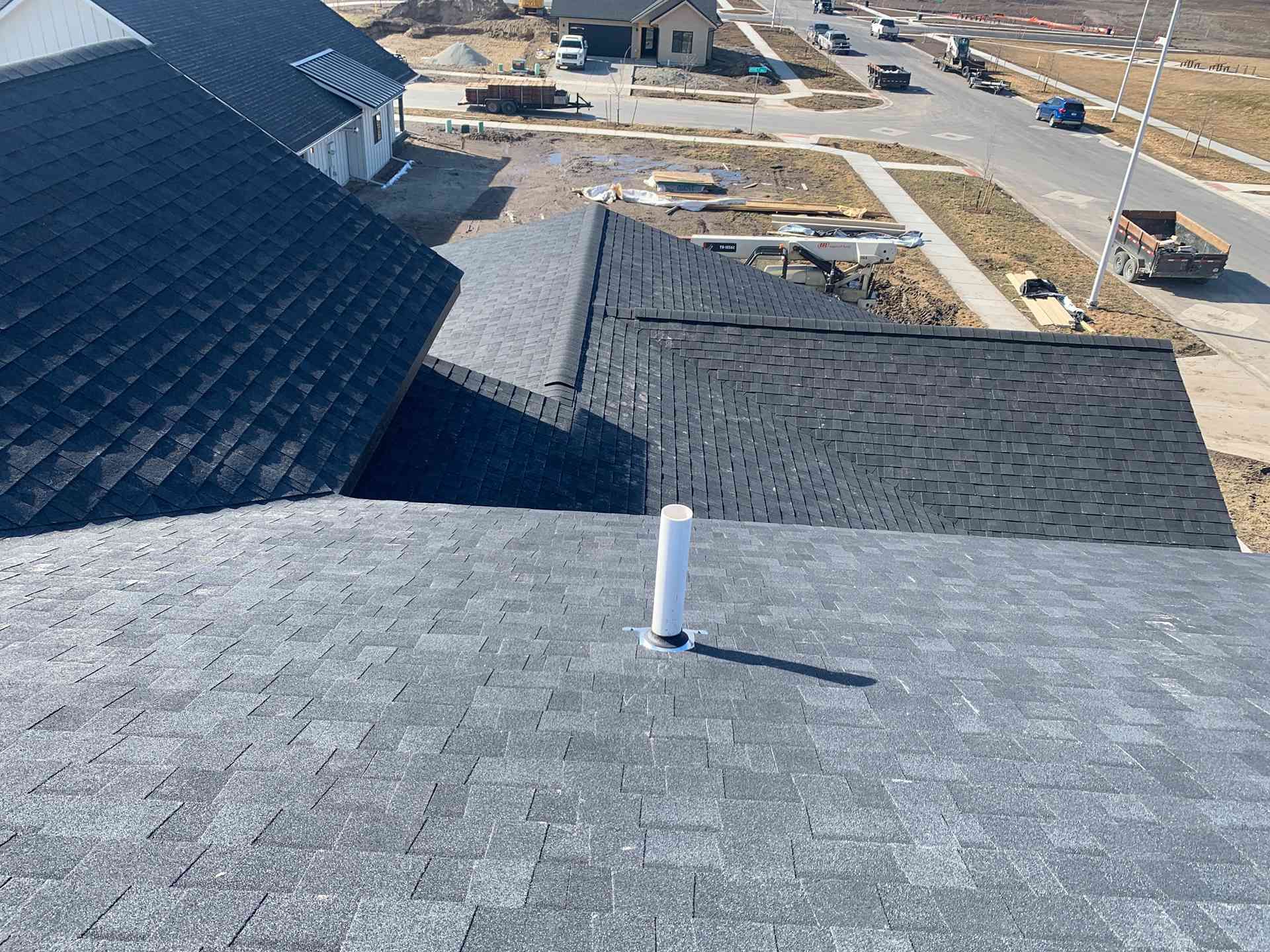 Rooftop view of gray shingles with a white vent pipe, overlooking a residential street and houses