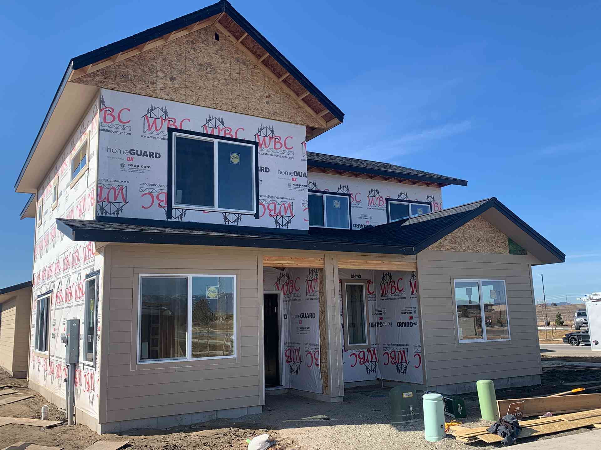 Two-story house under construction with white wrap, beige siding, and blue trim on a sunny day