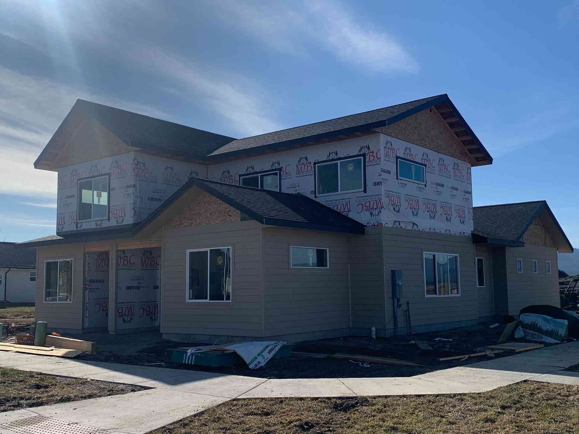 Two-story house under construction with tan siding, stone facade, and blue sky overhead