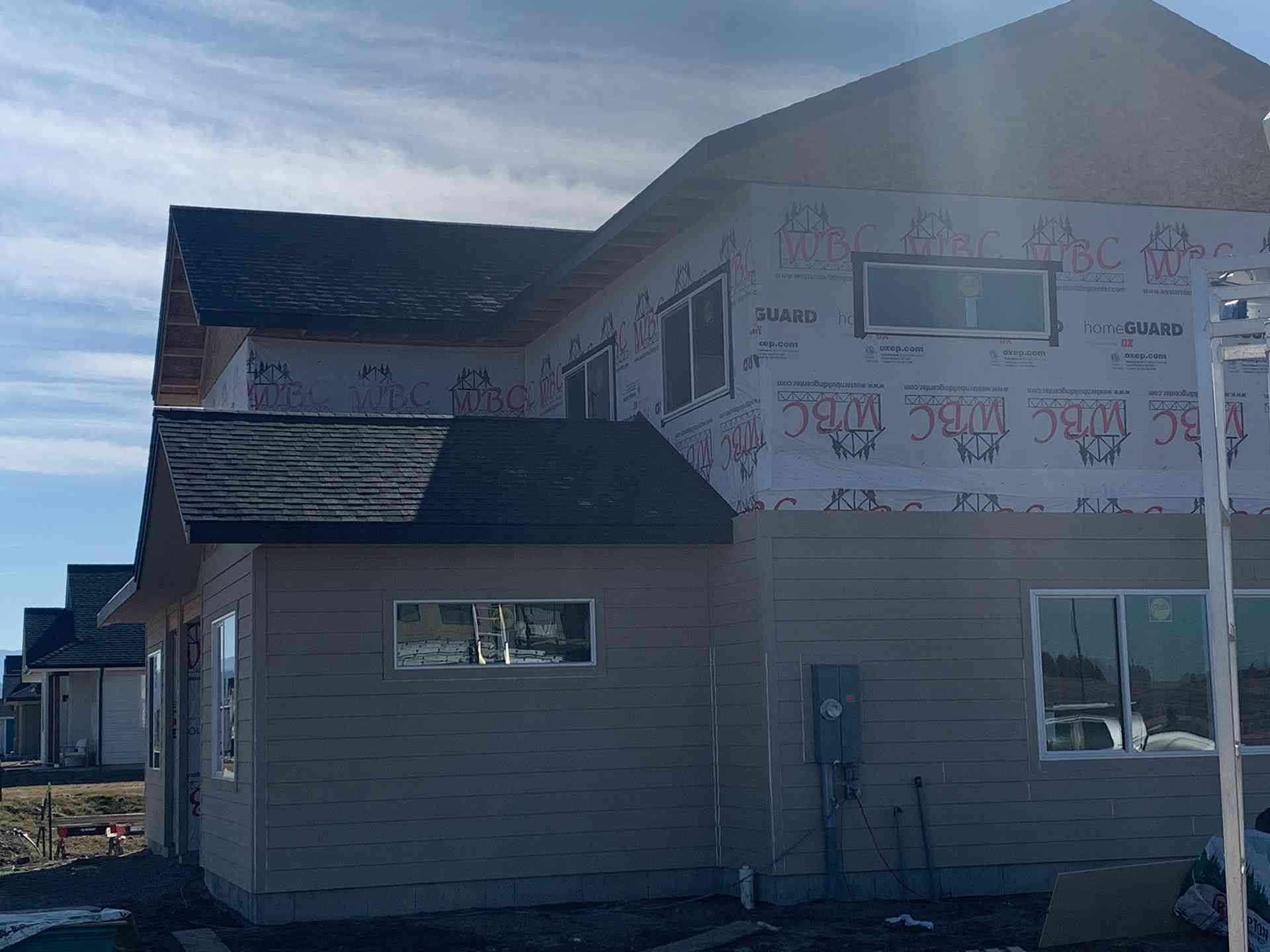 Partially built house with wrapped exterior, dark roof, and a bright sky overhead