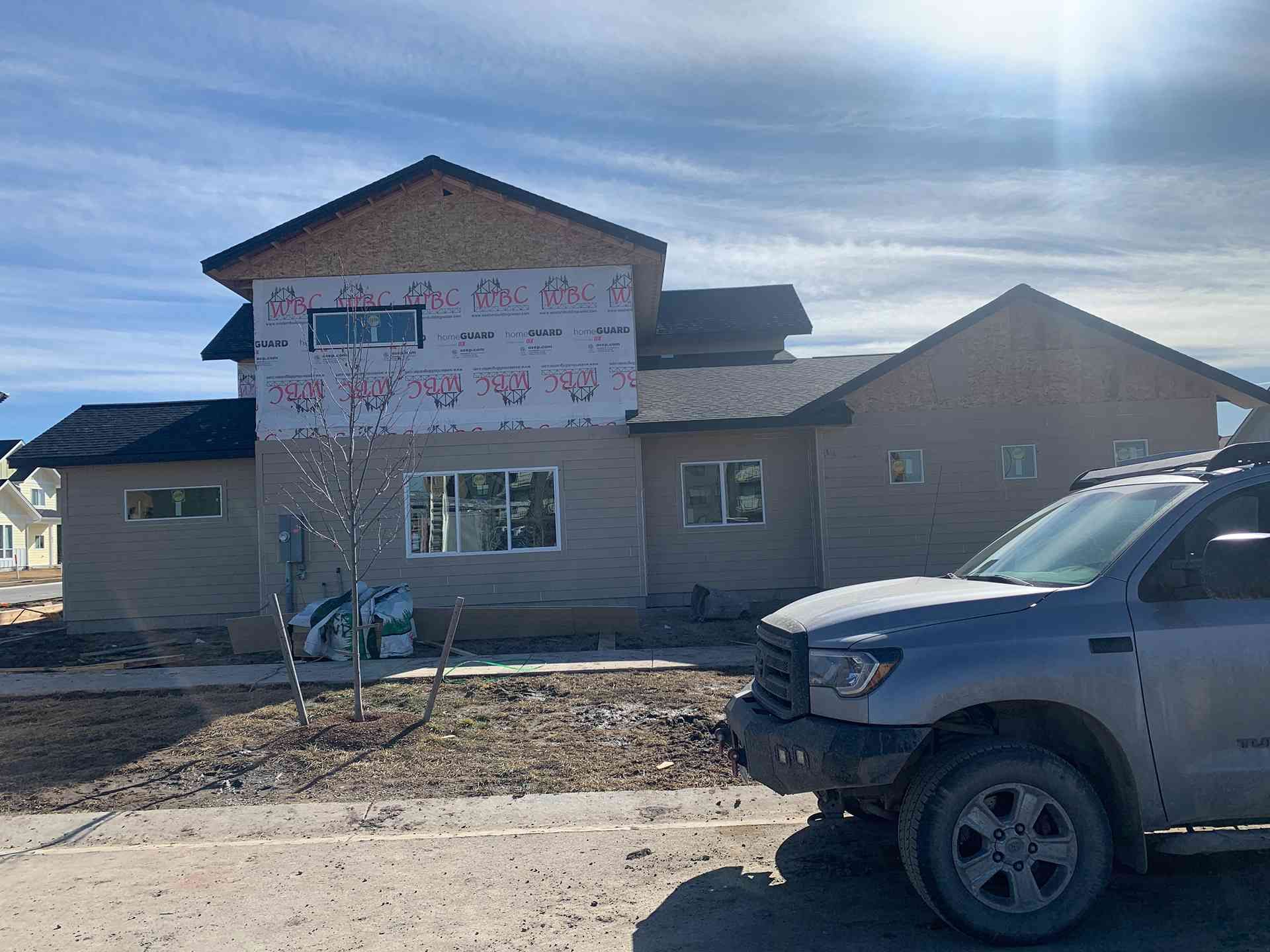 Partially built house with exposed wrap and windows, parked pickup truck in front under a cloudy sky