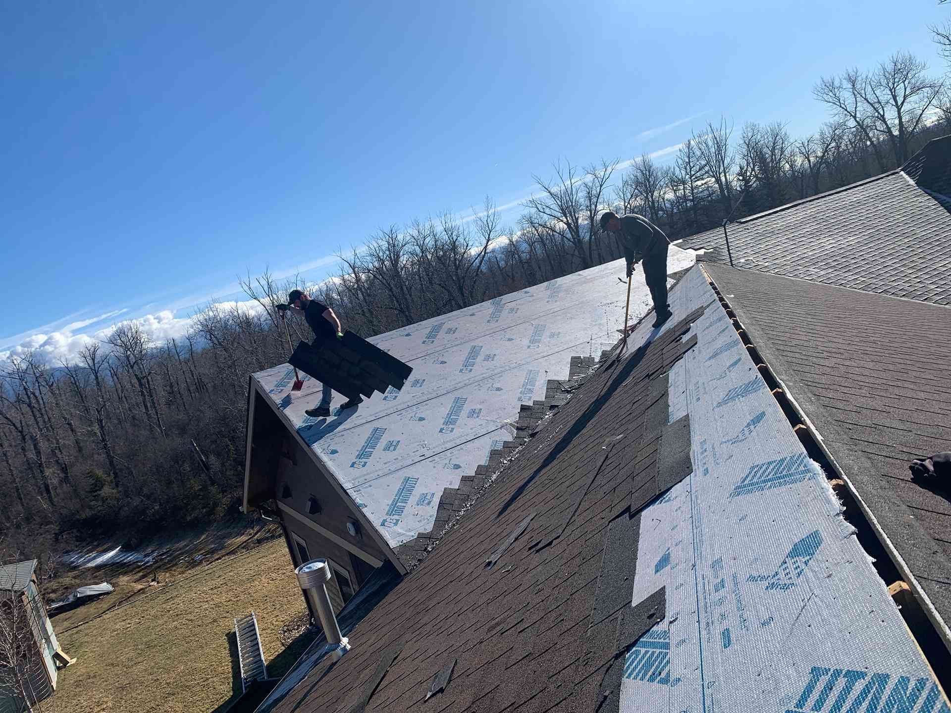 Workers installing roofing underlayment on a steep house roof on a clear day