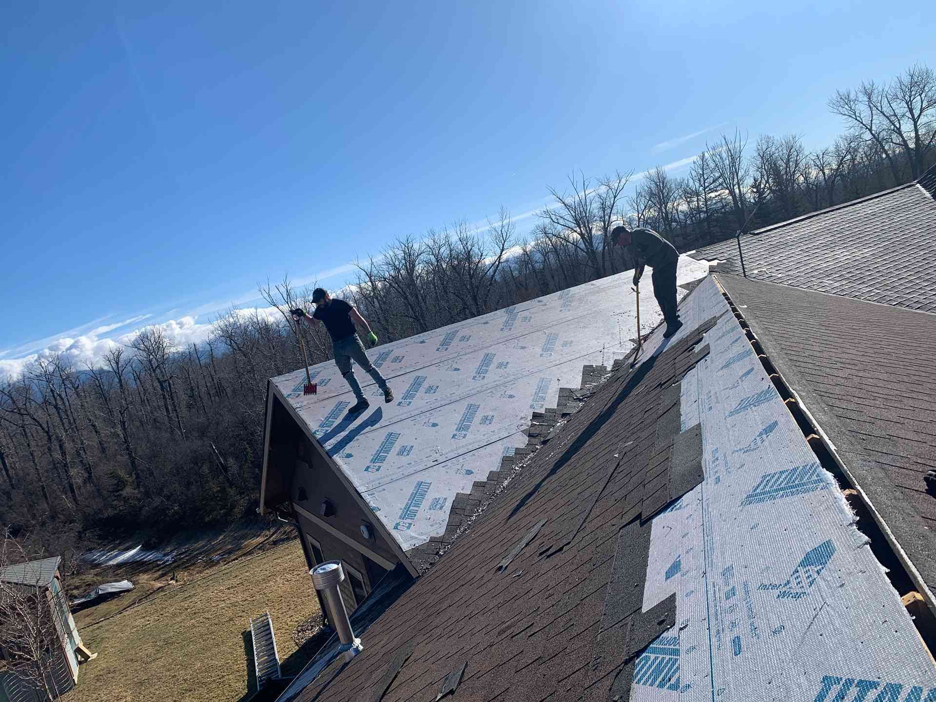Workers on a steep roof installing underlayment on a sunny day