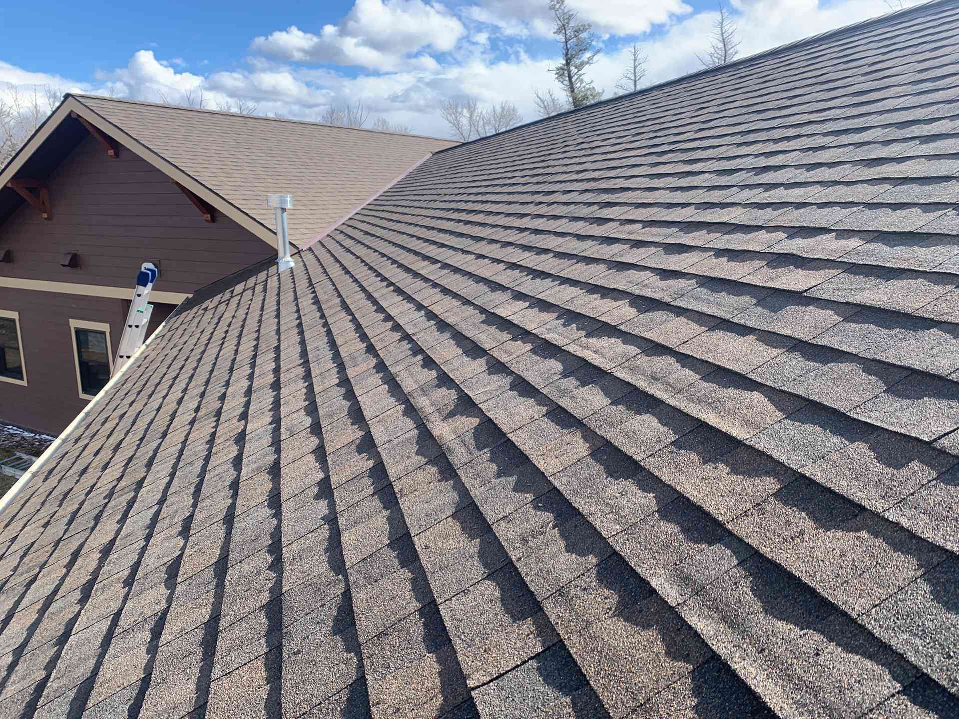 Close-up of a gray shingled roof with a neighboring house and blue sky in the background