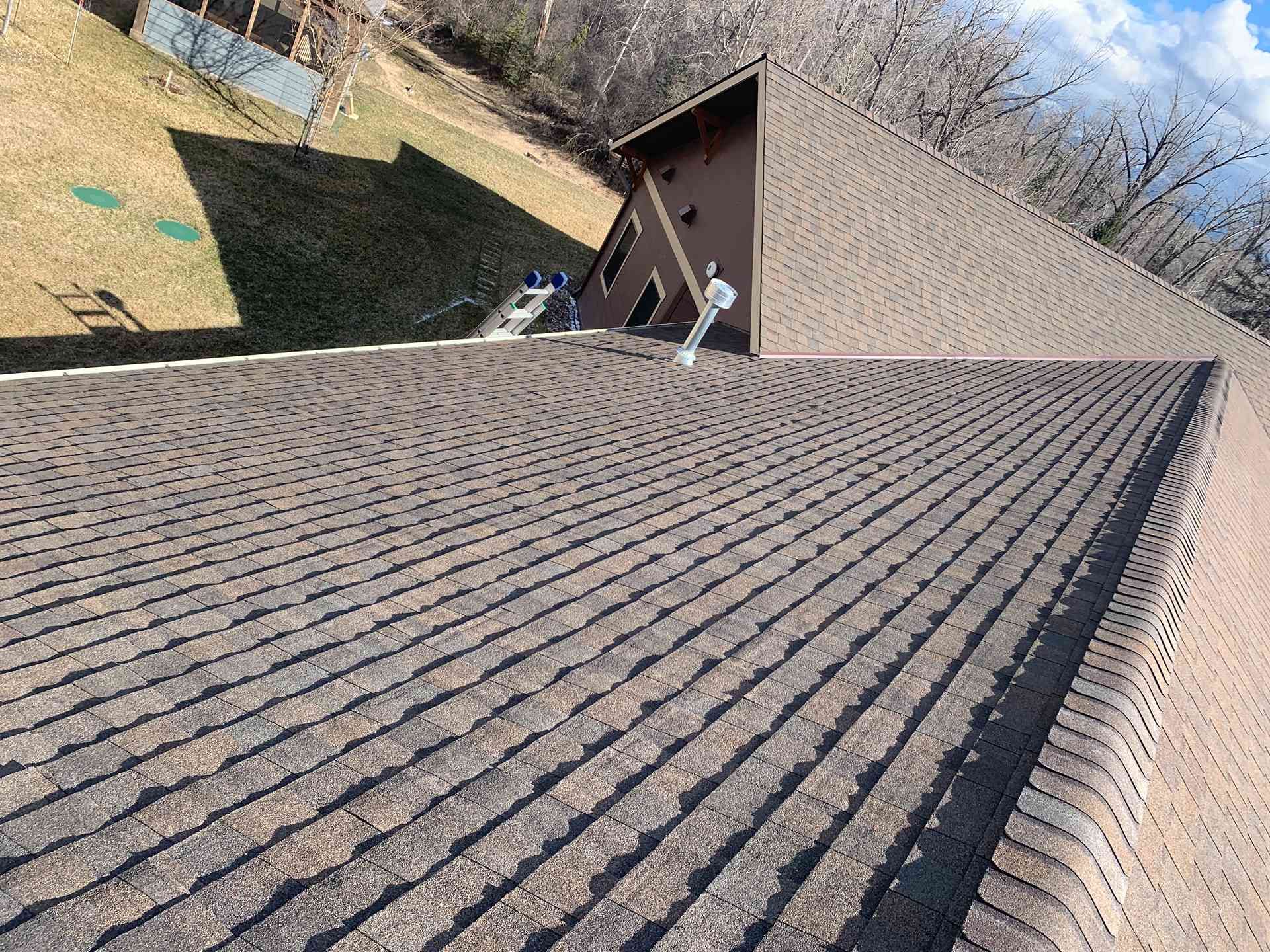 Tilted view of a shingled roof with a house gable and yard below on a clear day