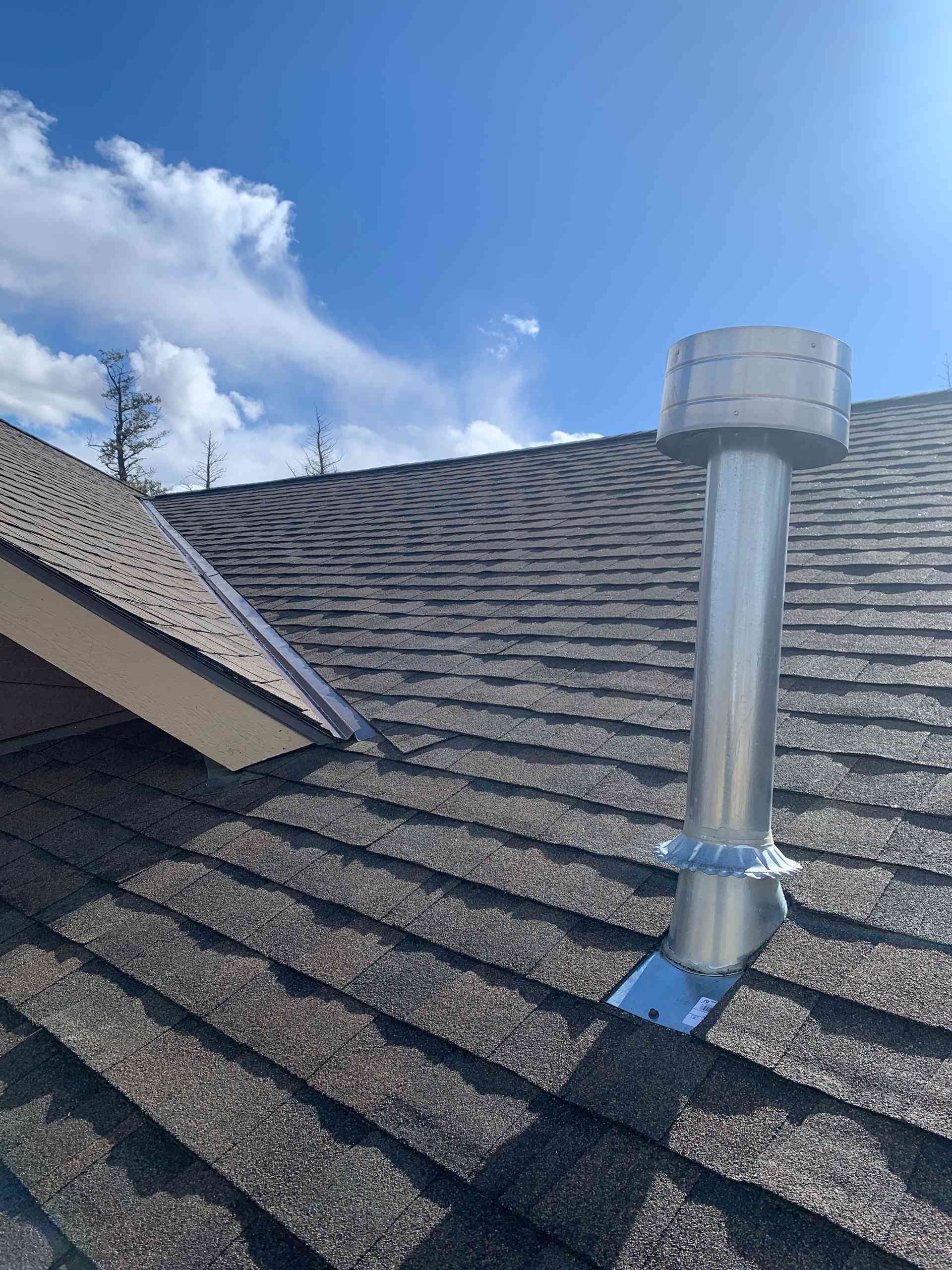 Rooftop with a metal vent pipe under a bright blue sky with clouds