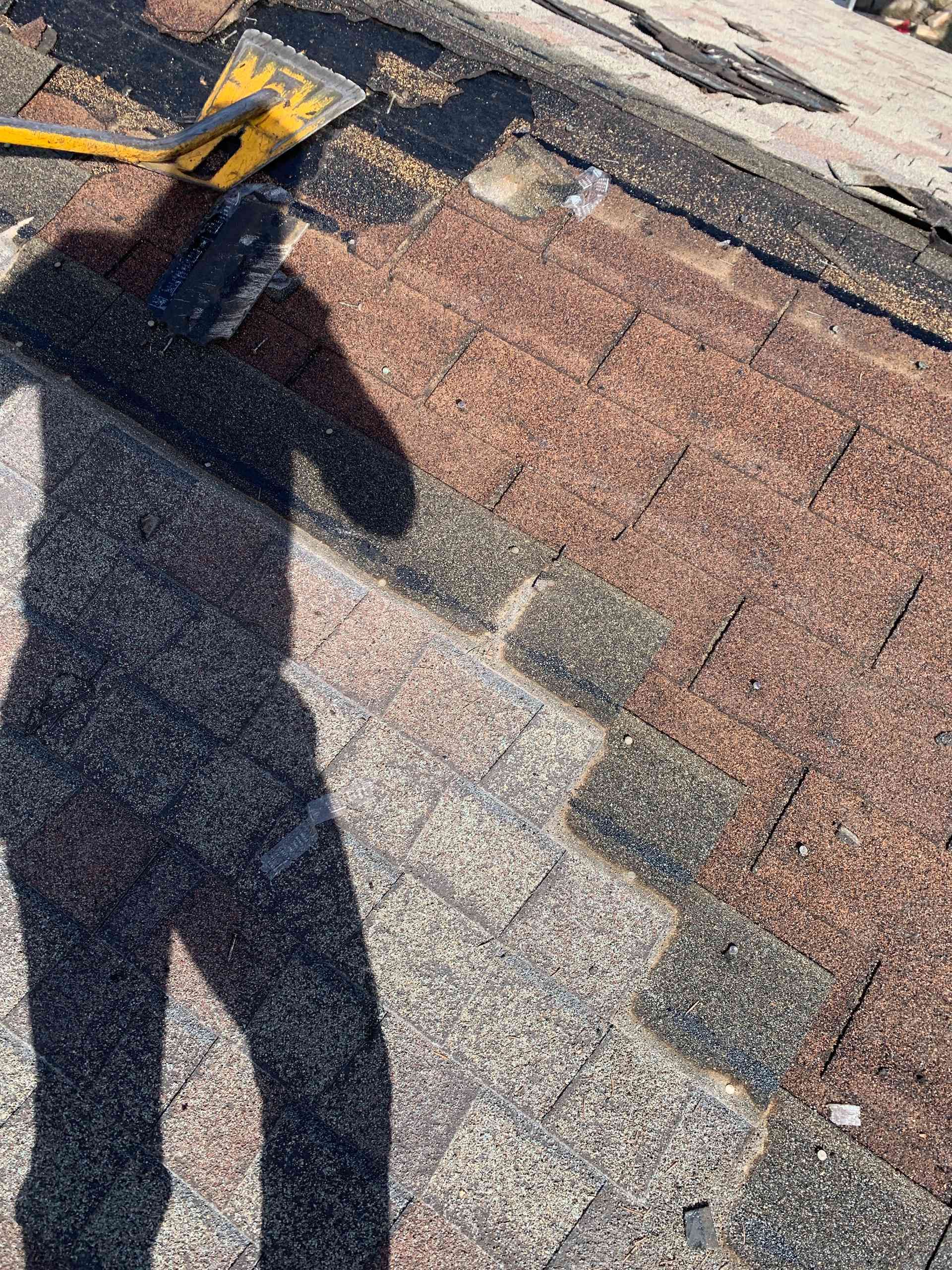 Shingled rooftop with a shadowed person holding a yellow-handled tool near the top edge.