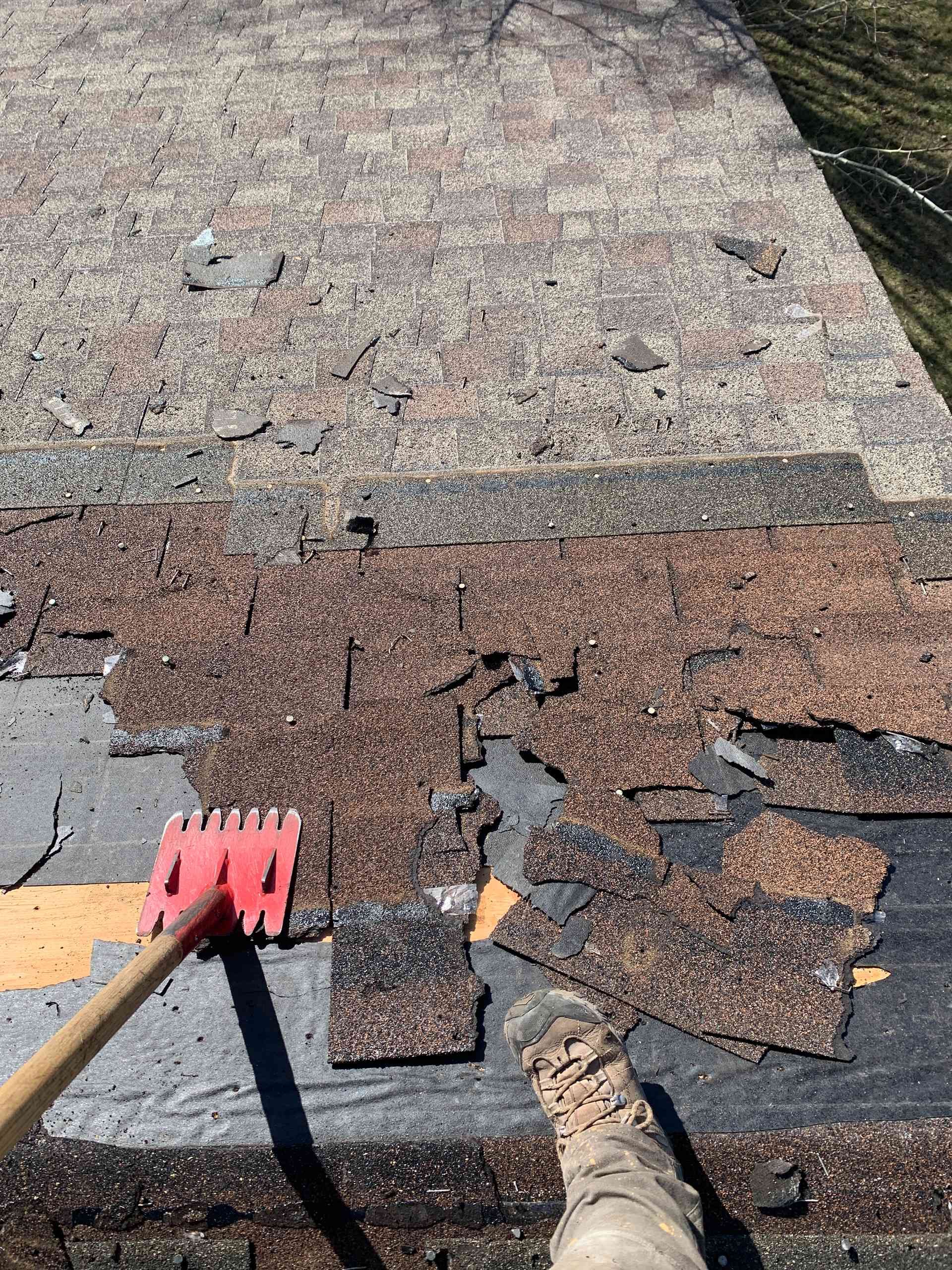 Rotted roof shingles being removed, with a red roofing tool and a boot on the roof.