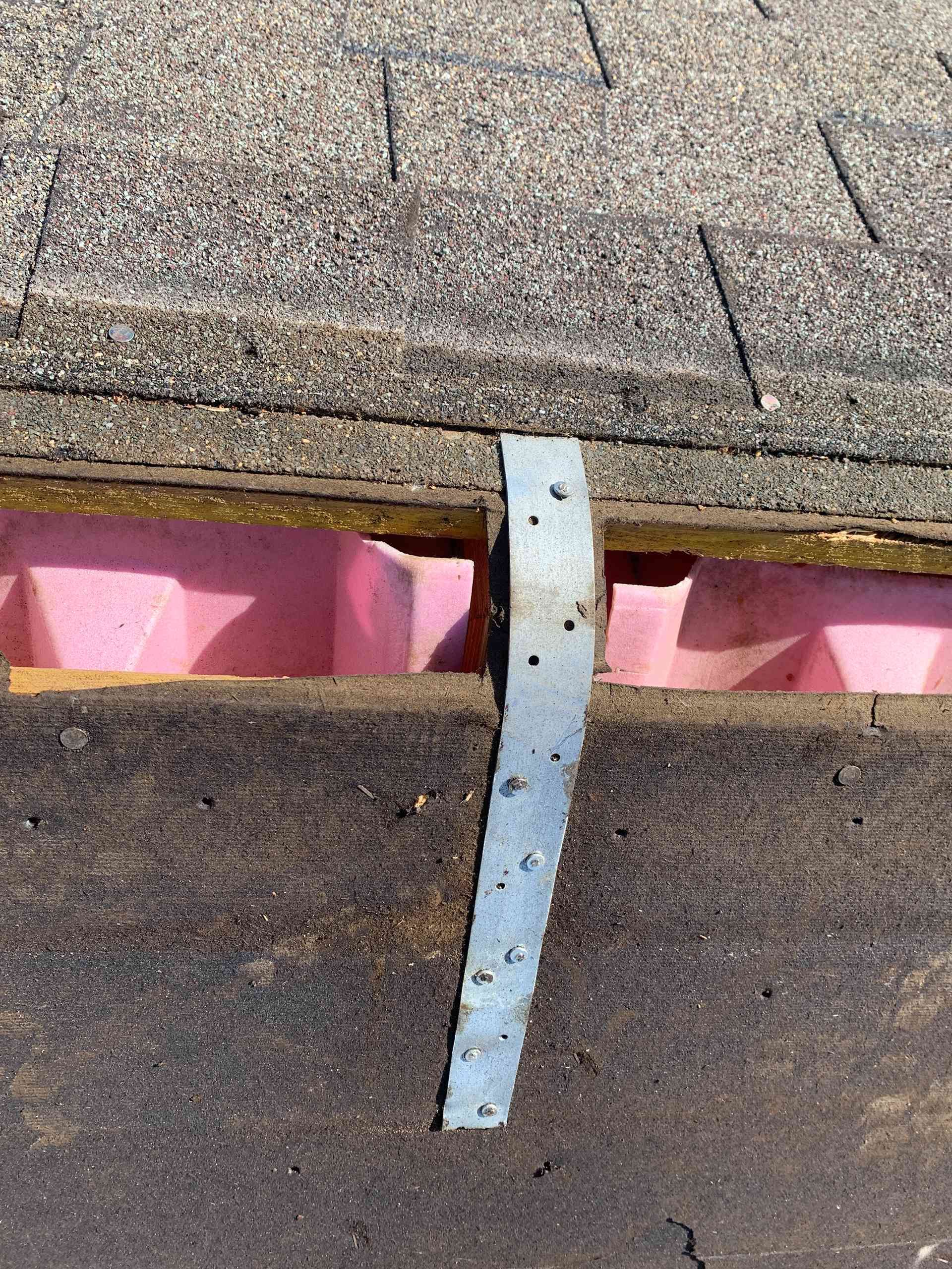 Close-up of a roof seam with a metal flashing strip and pink underlayment exposed between shingles