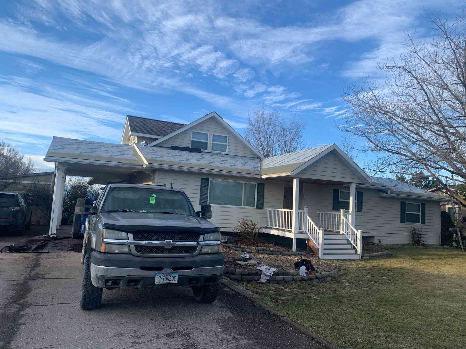 Silver pickup truck parked in driveway beside a light-gray house with a front porch and leafless trees