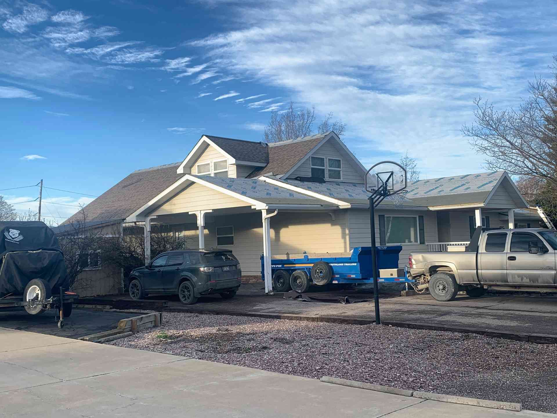Suburban house with parked vehicles and a basketball hoop under a clear blue sky