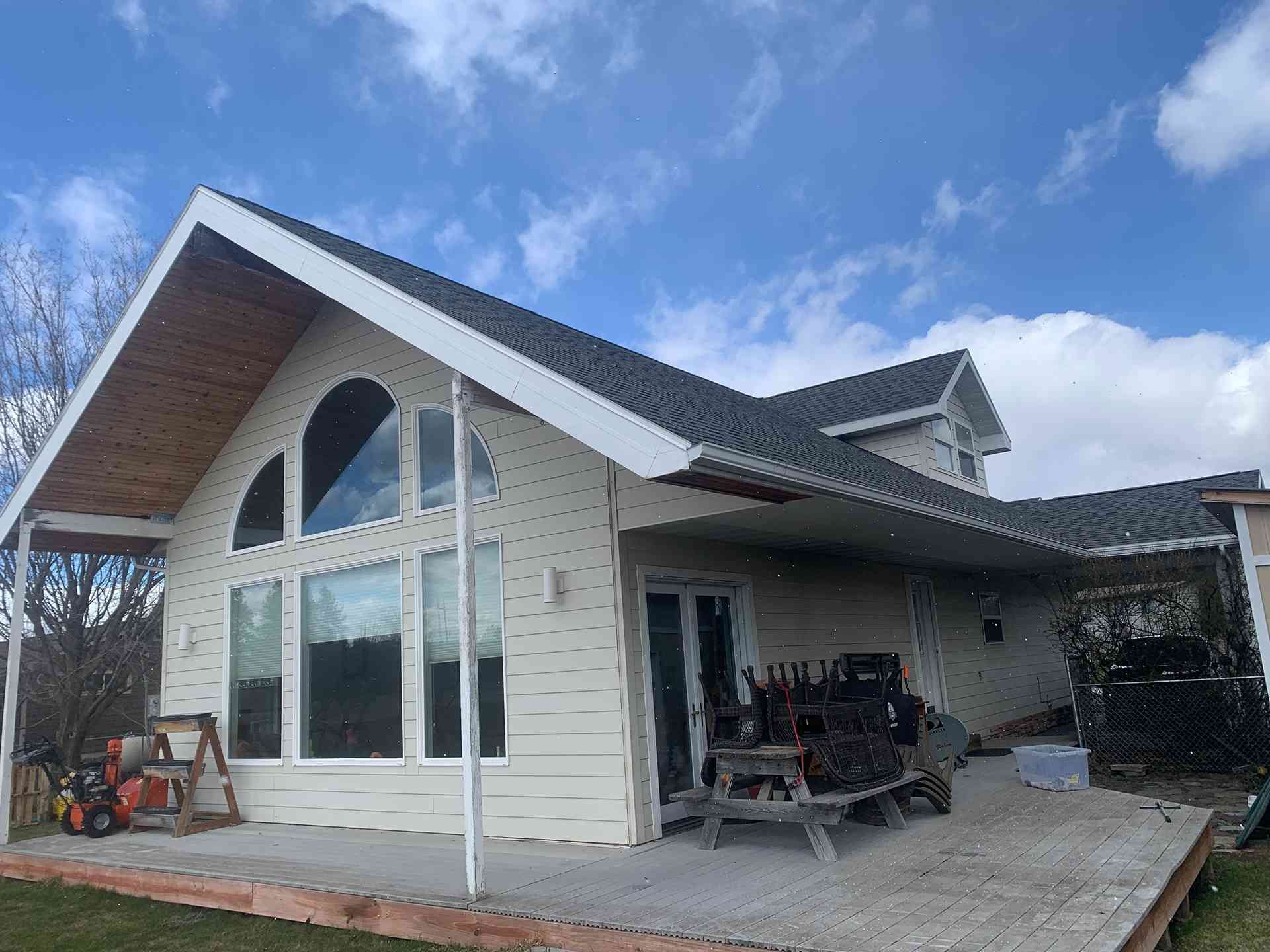Modern house exterior with a large arched window, white siding, dark roof, and a covered patio under a blue sky