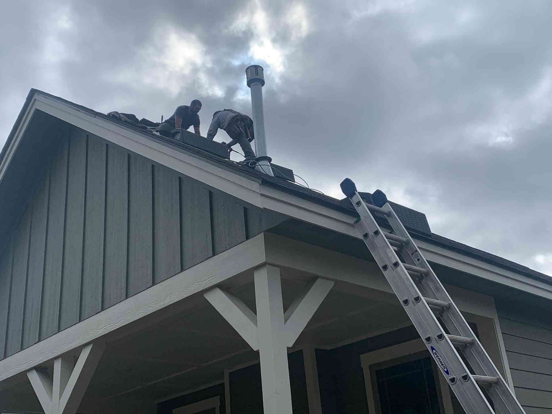 Workers on a roof using a ladder under a cloudy sky, with a house chimney visible.