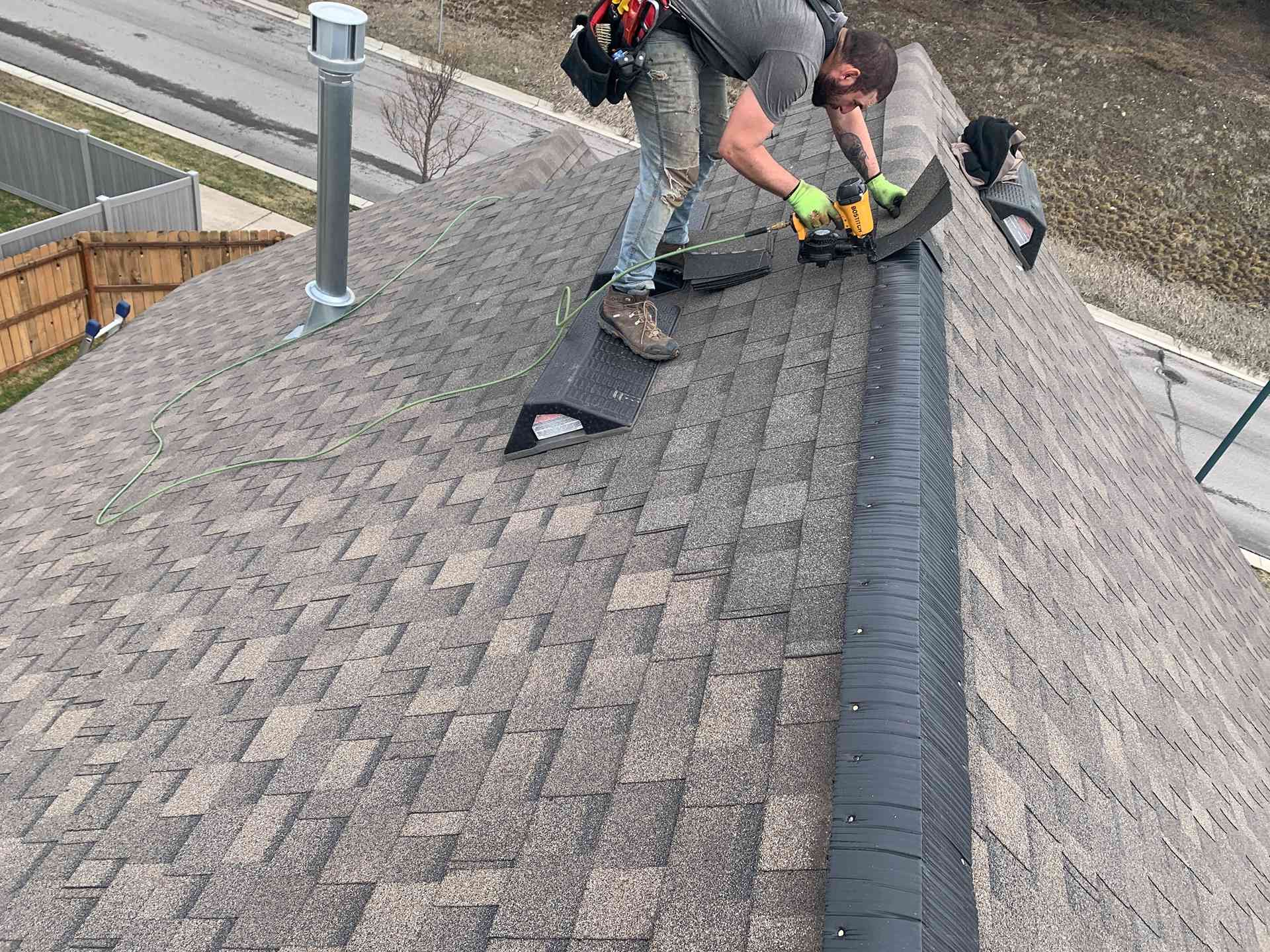 Workers repairing a shingled roof beside a black ridge vent and chimney
