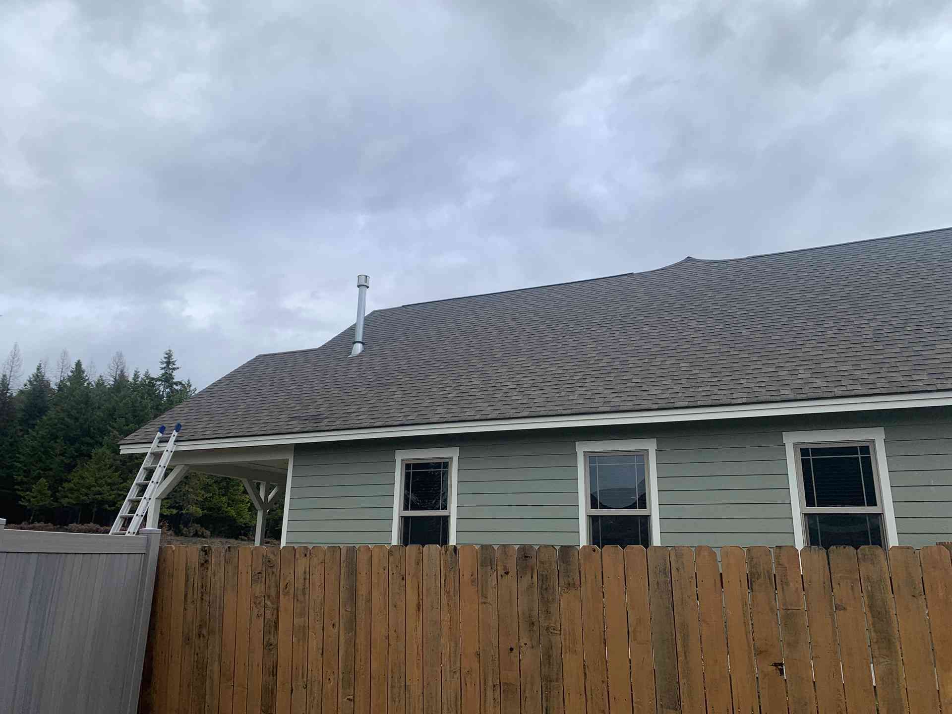 Single-story house with a wavy roof, ladder, and wooden fence under a cloudy sky