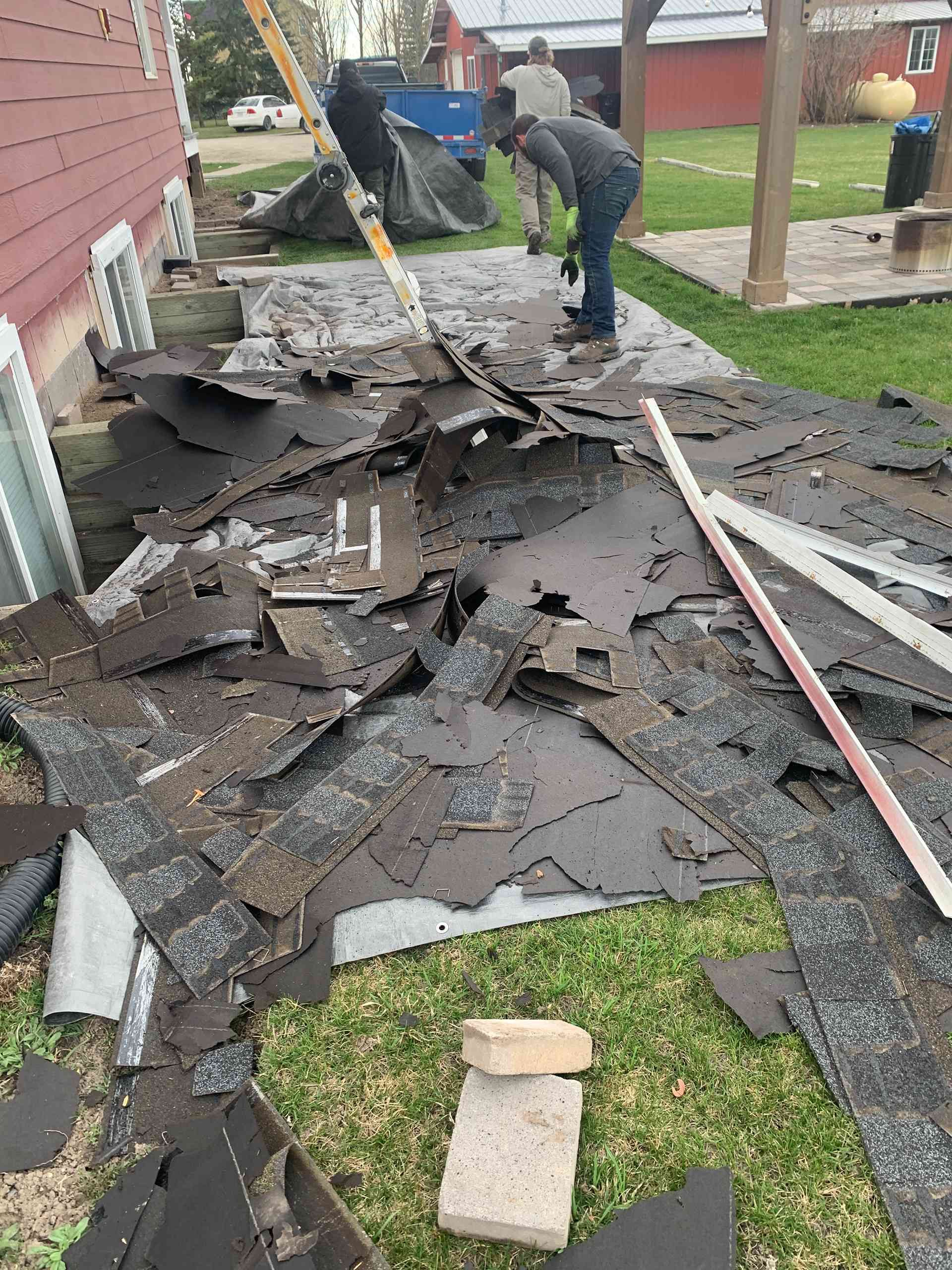 Worker clearing debris from a collapsed roof beside a house and yard