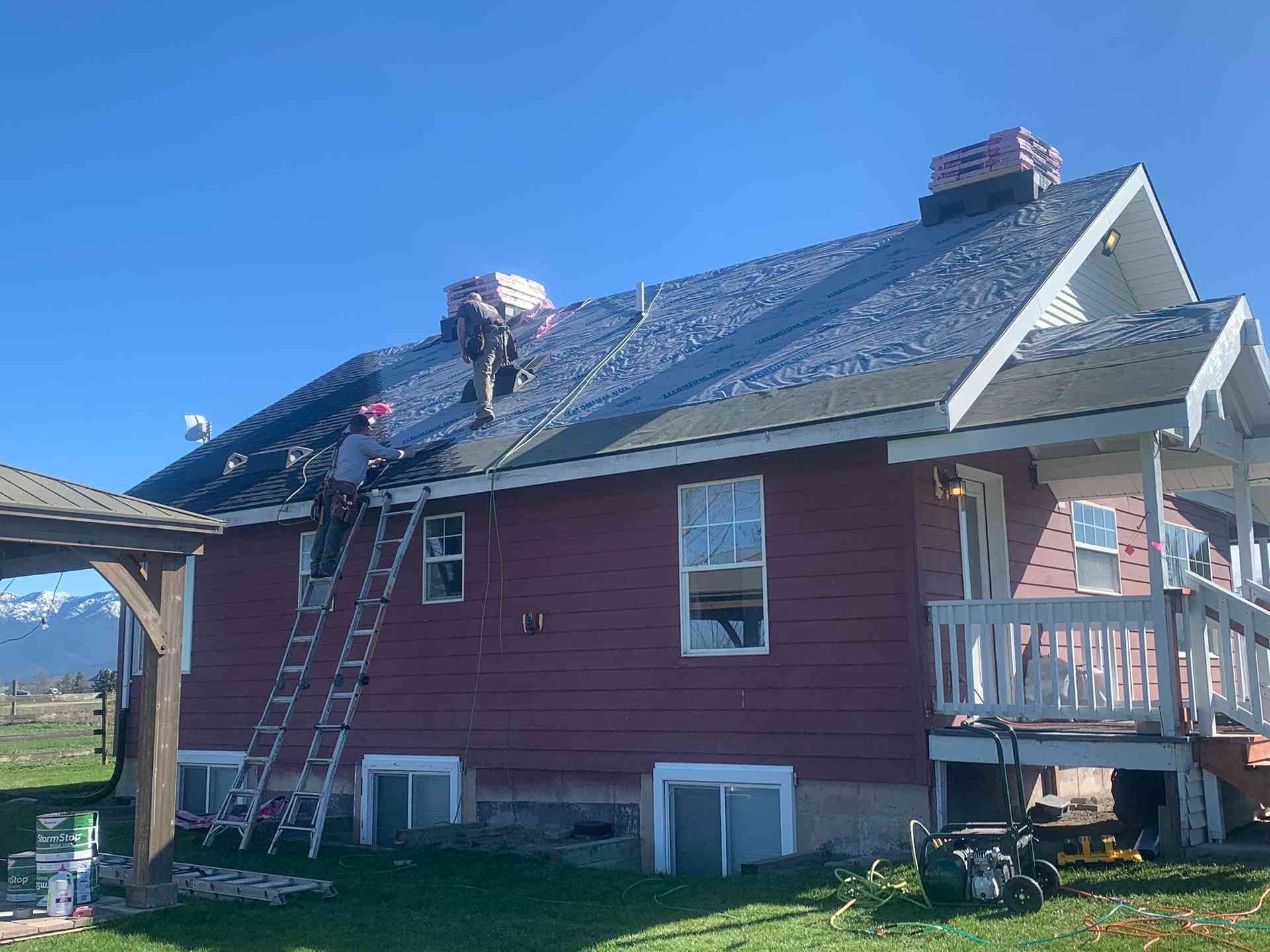 House roof under repair with two ladders, solar panels, and chimney work on a sunny day