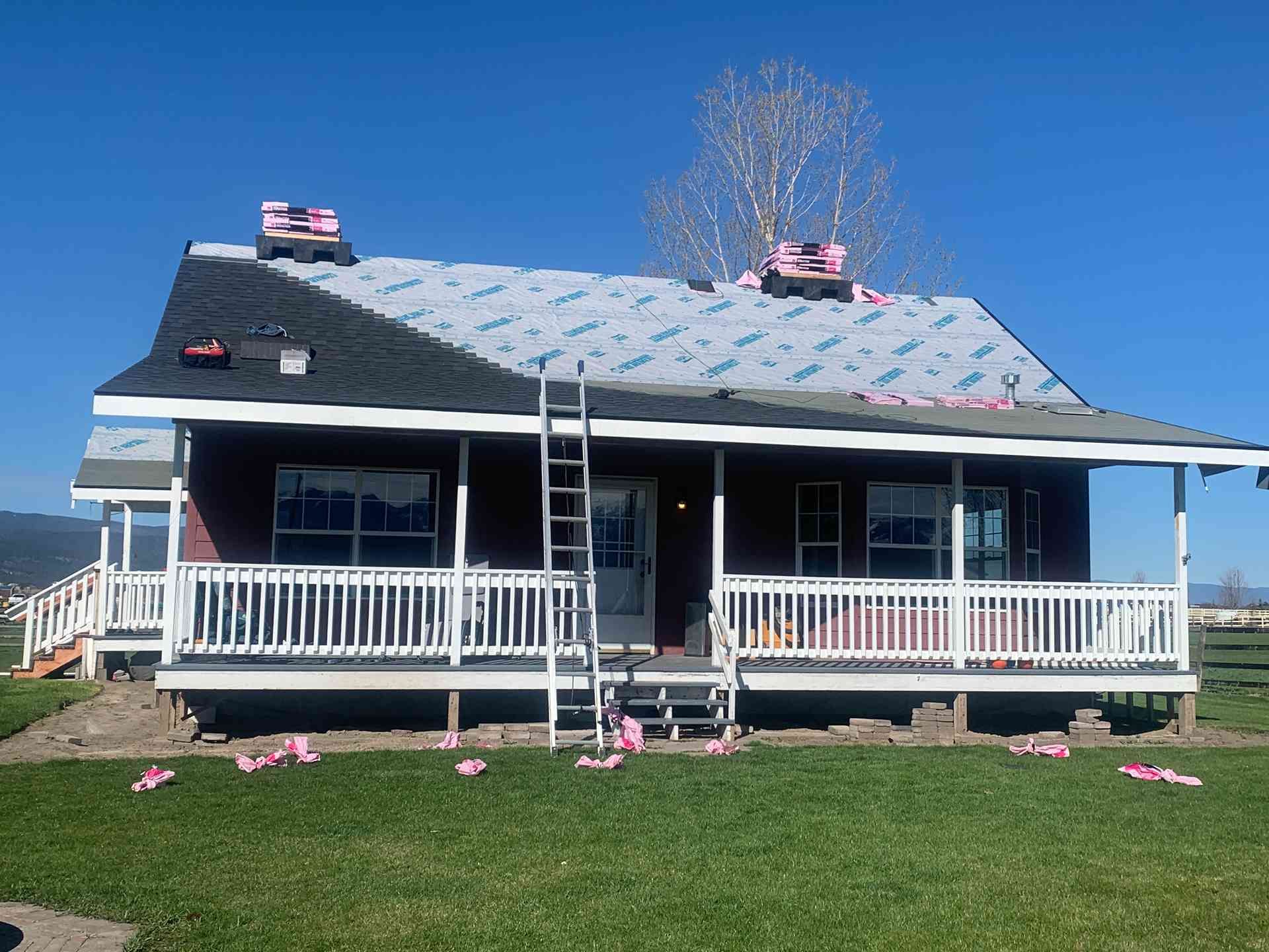 A house with a white porch, dark roof, and ladder leaning against the front under a clear blue sky.