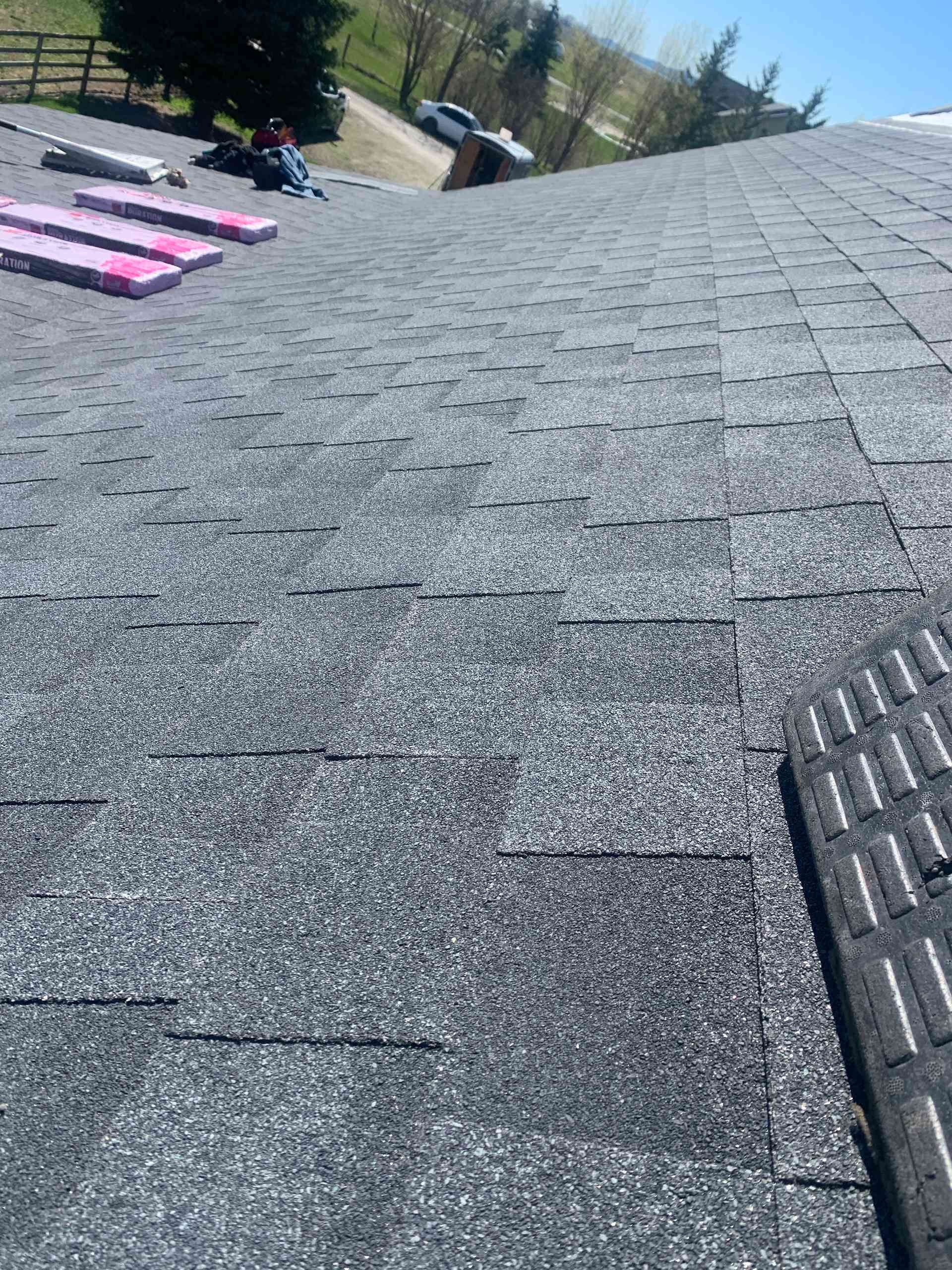 Roofer’s view of a shingled roof with stacked pink materials and a vent on the right.
