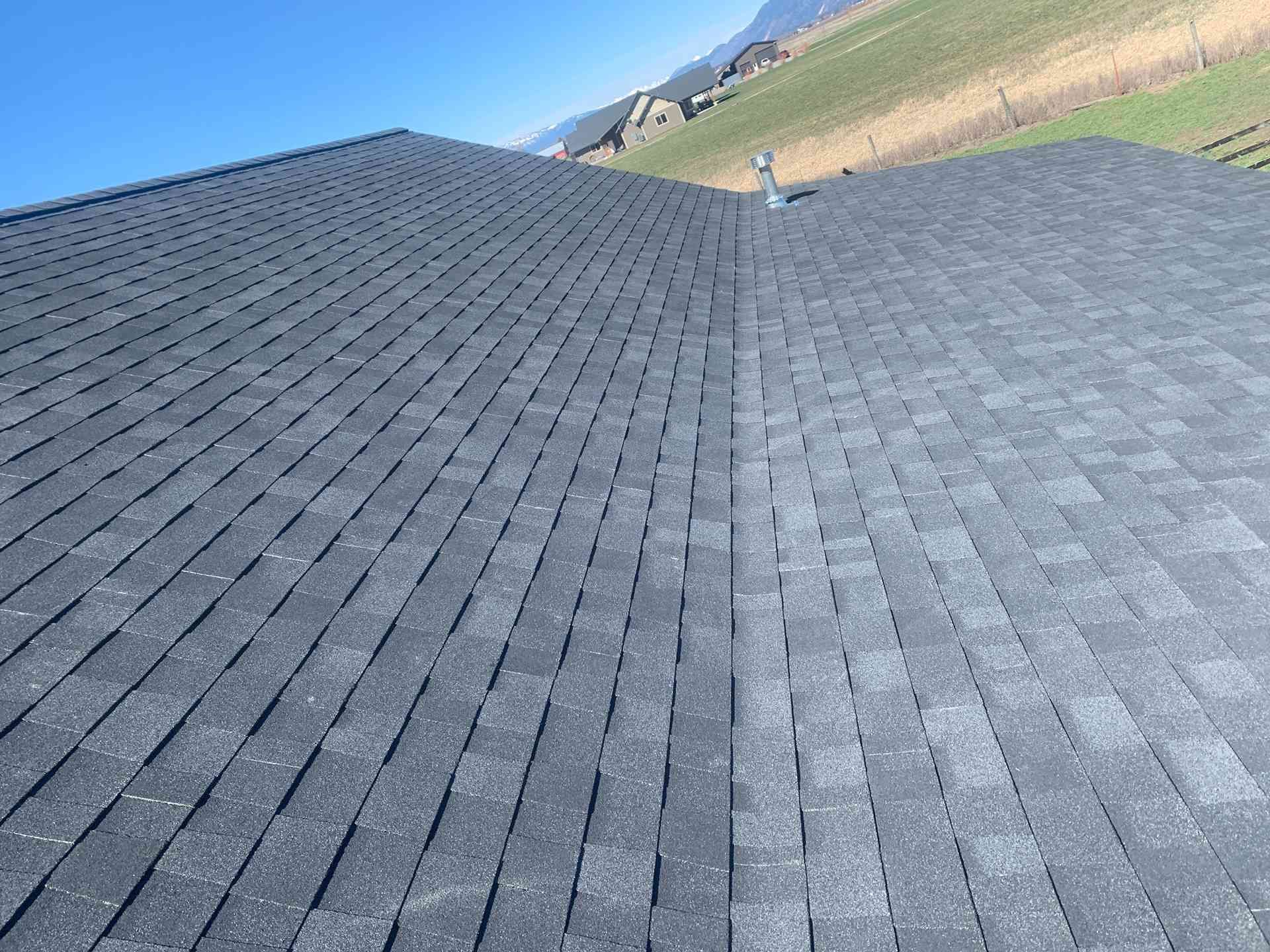 Gray shingled roof with a central ridge, viewed toward distant mountains under a blue sky