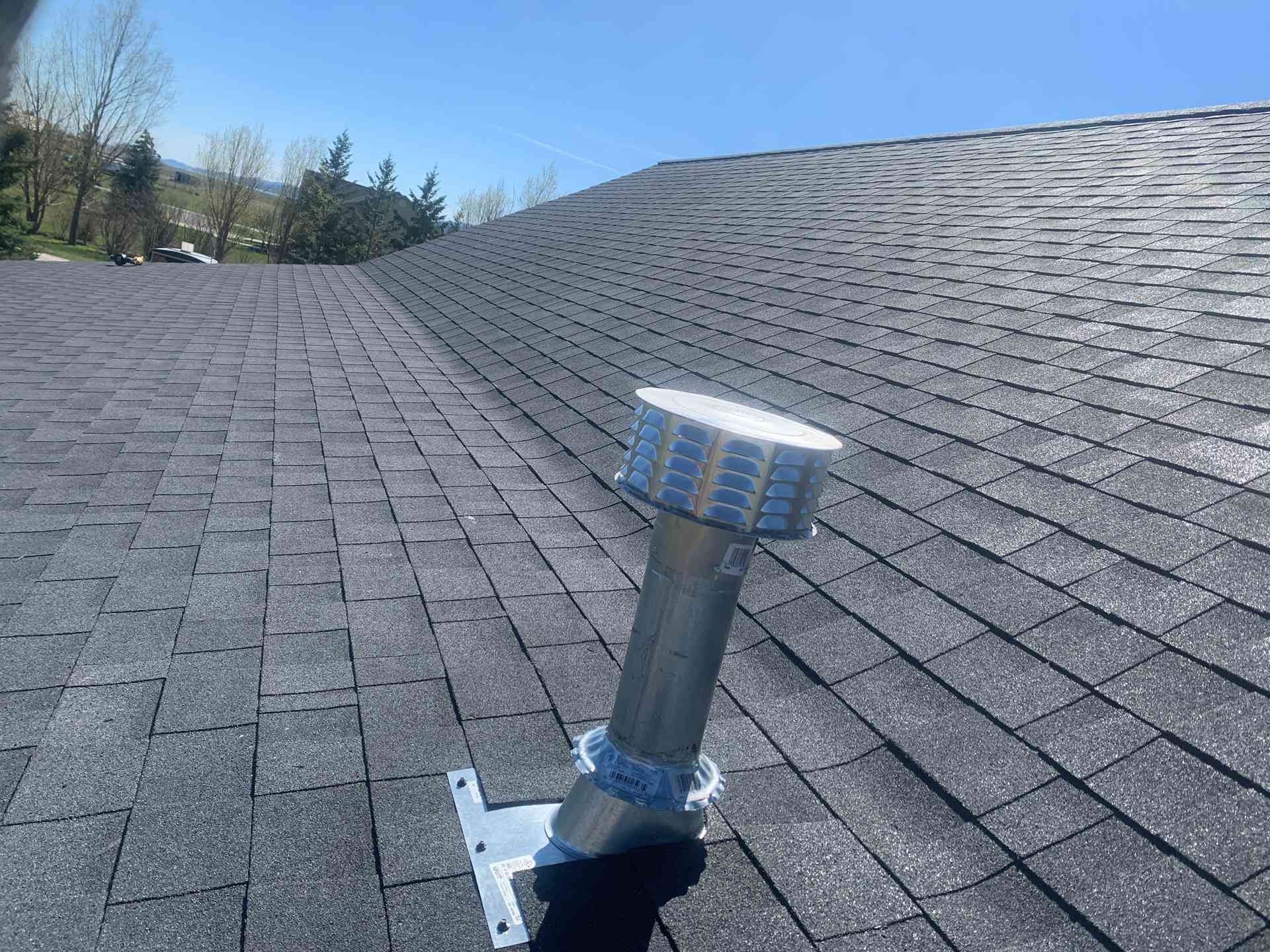 Roof with a silver vent pipe and cap against a clear blue sky