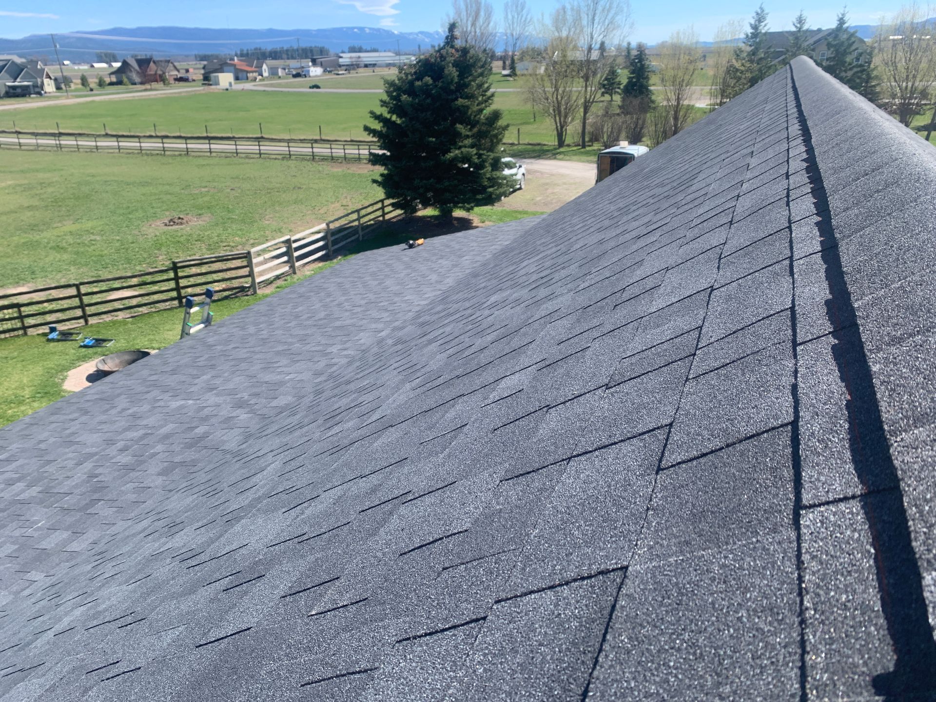 Shingled roof overlooking a fenced green pasture and distant mountains on a clear day