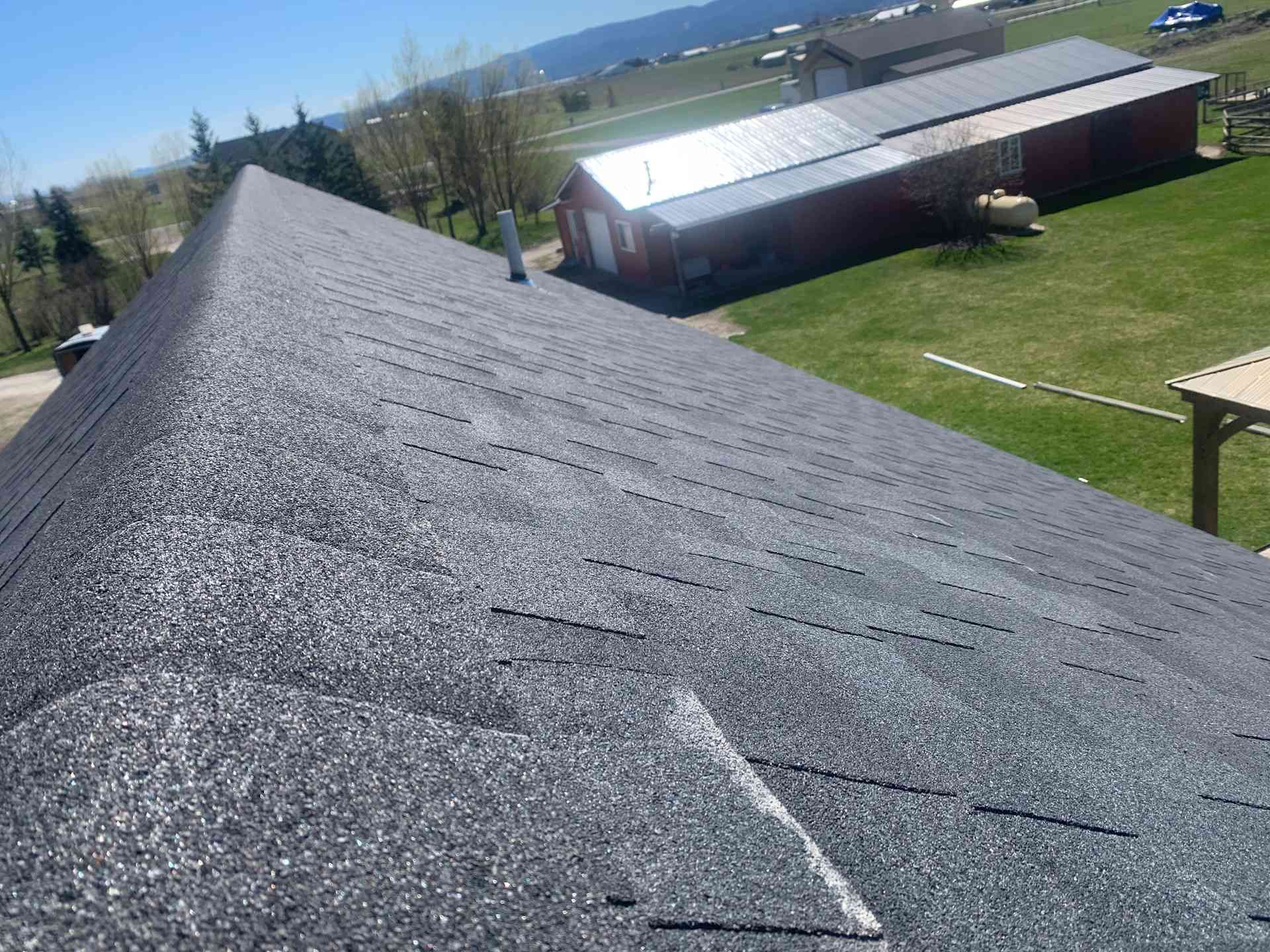 Roof shingles on a sloped rooftop overlooking grassy buildings and distant hills under a clear sky