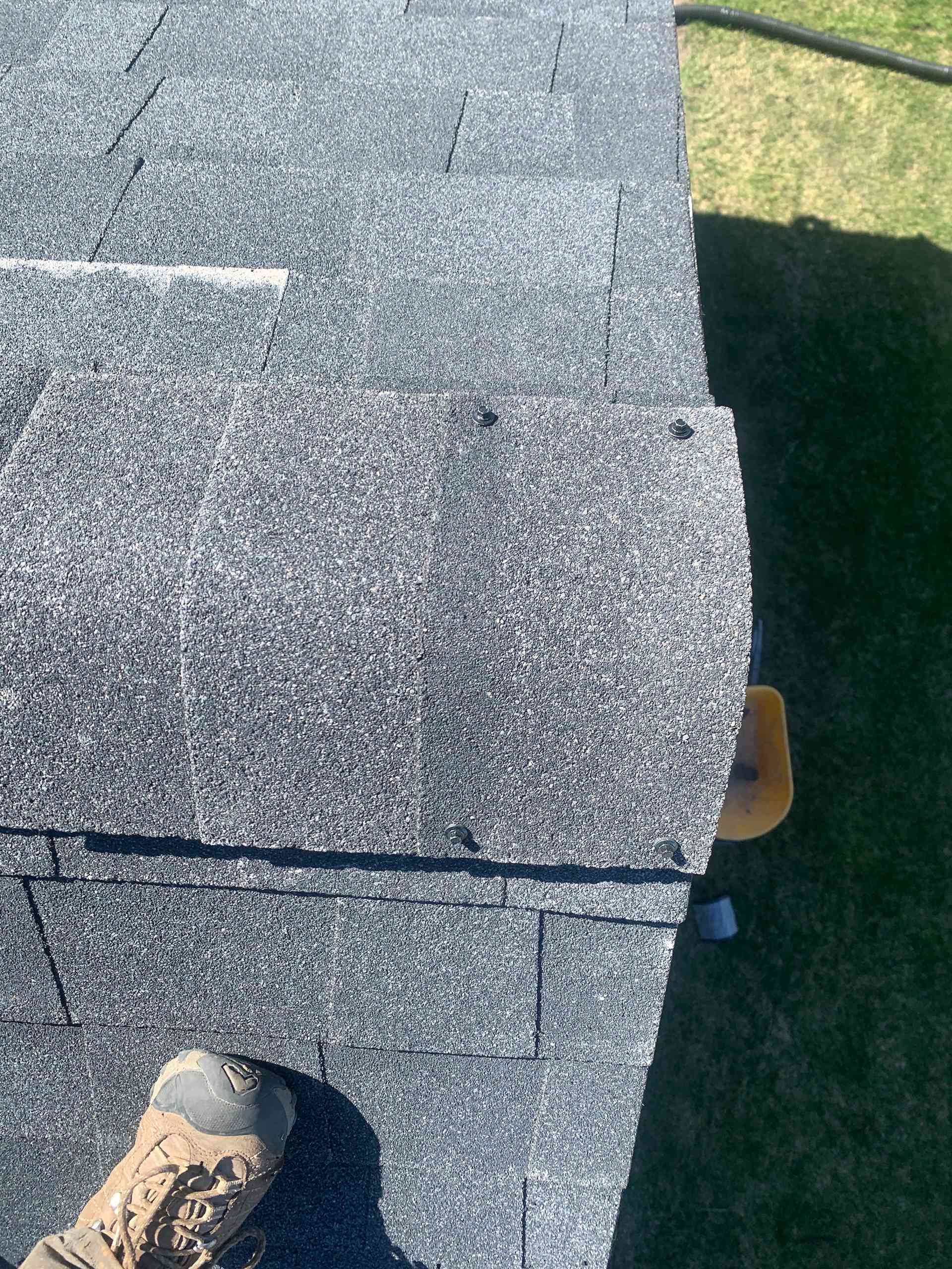 Foot on gray shingled roof edge beside green grass and a shadow below