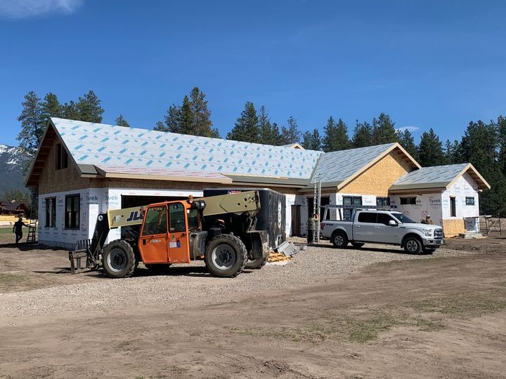 Construction site with unfinished white house, orange forklift, and silver pickup under a clear blue sky