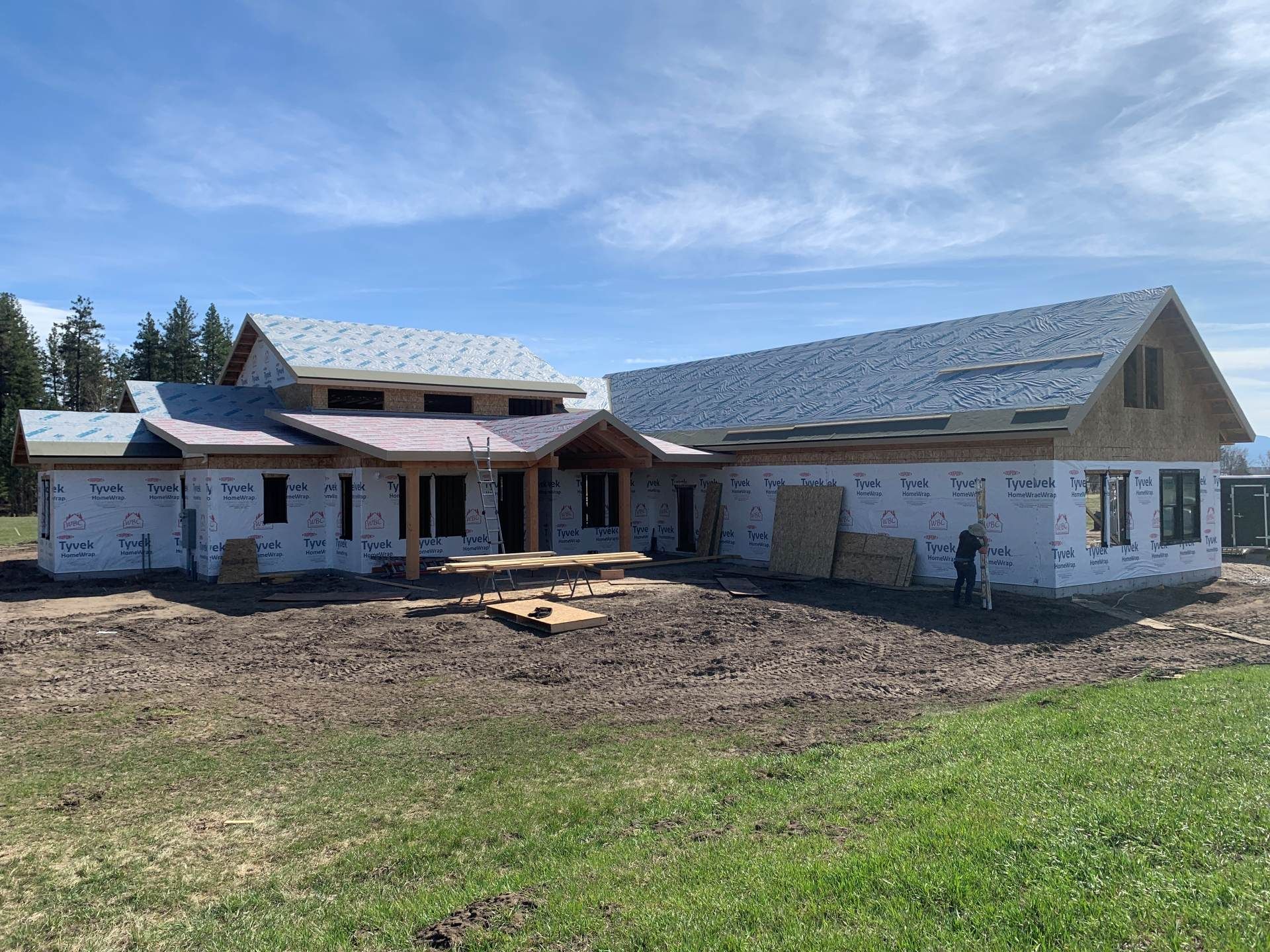 New house under construction with white sheathing, gray roof, and a dirt lot in front
