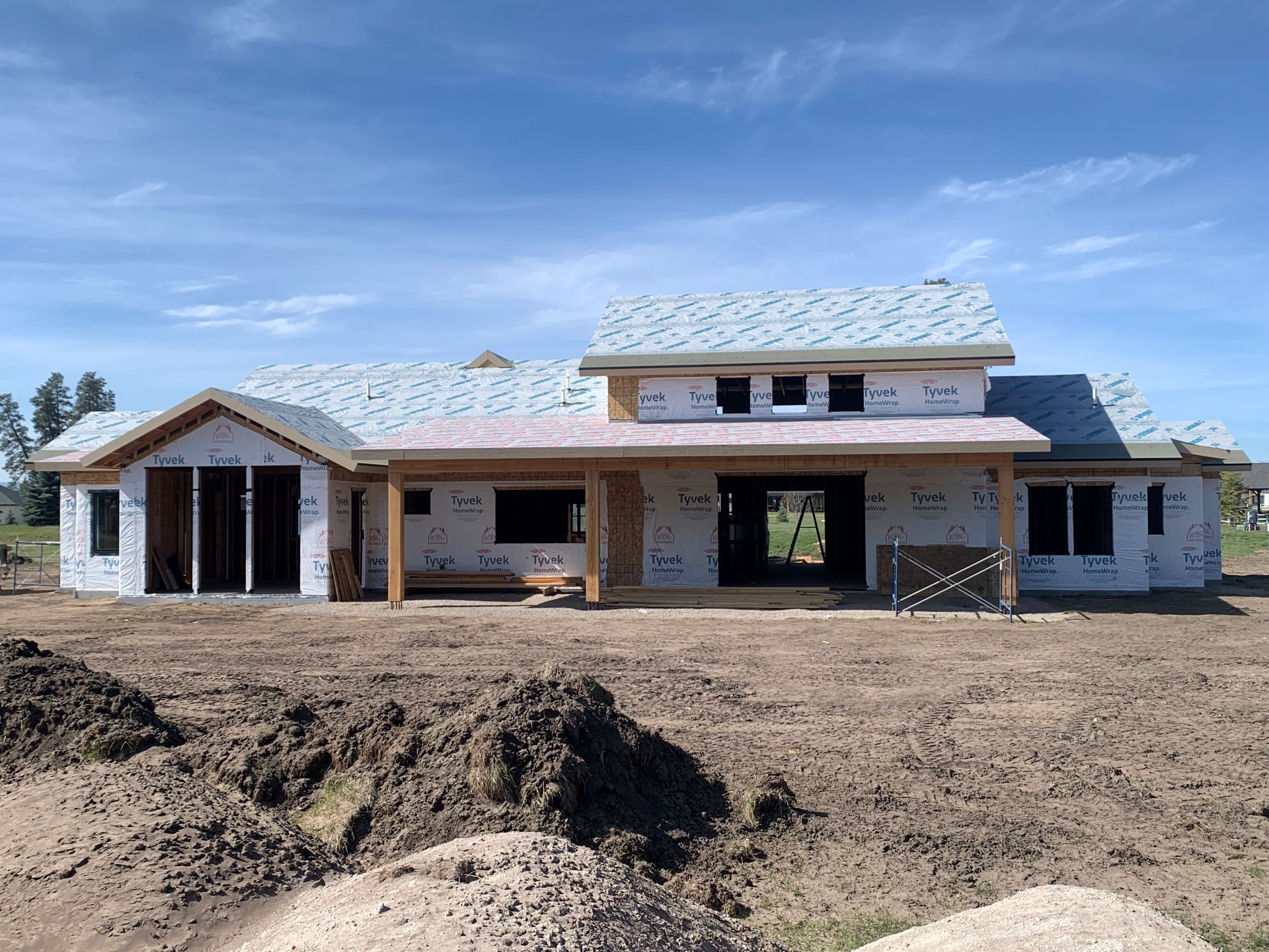 New house under construction with stone exterior and unfinished dirt lot under a blue sky