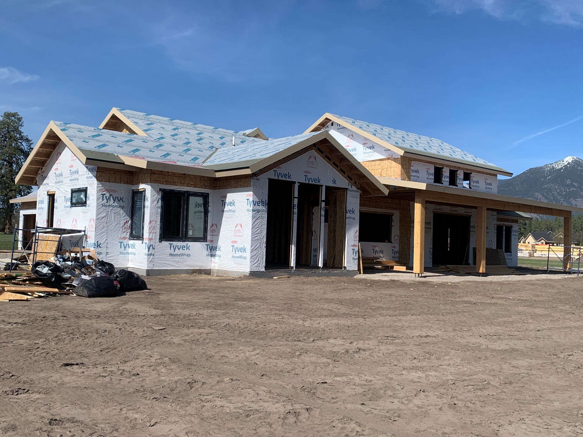 Partially built house with white walls, blue roof, and mountain backdrop under clear sky