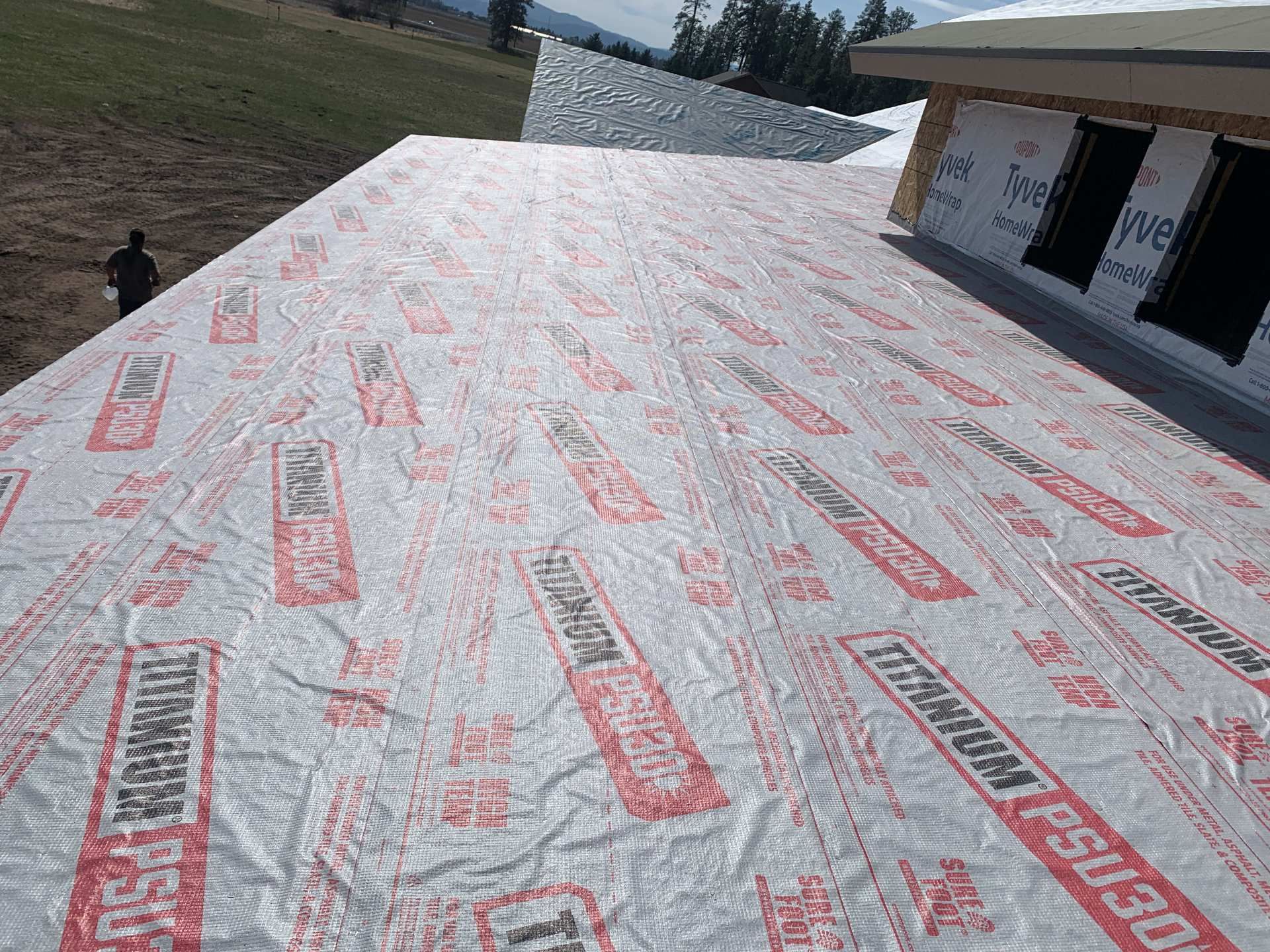 White roofing underlayment on a sloped roof beside a house under construction