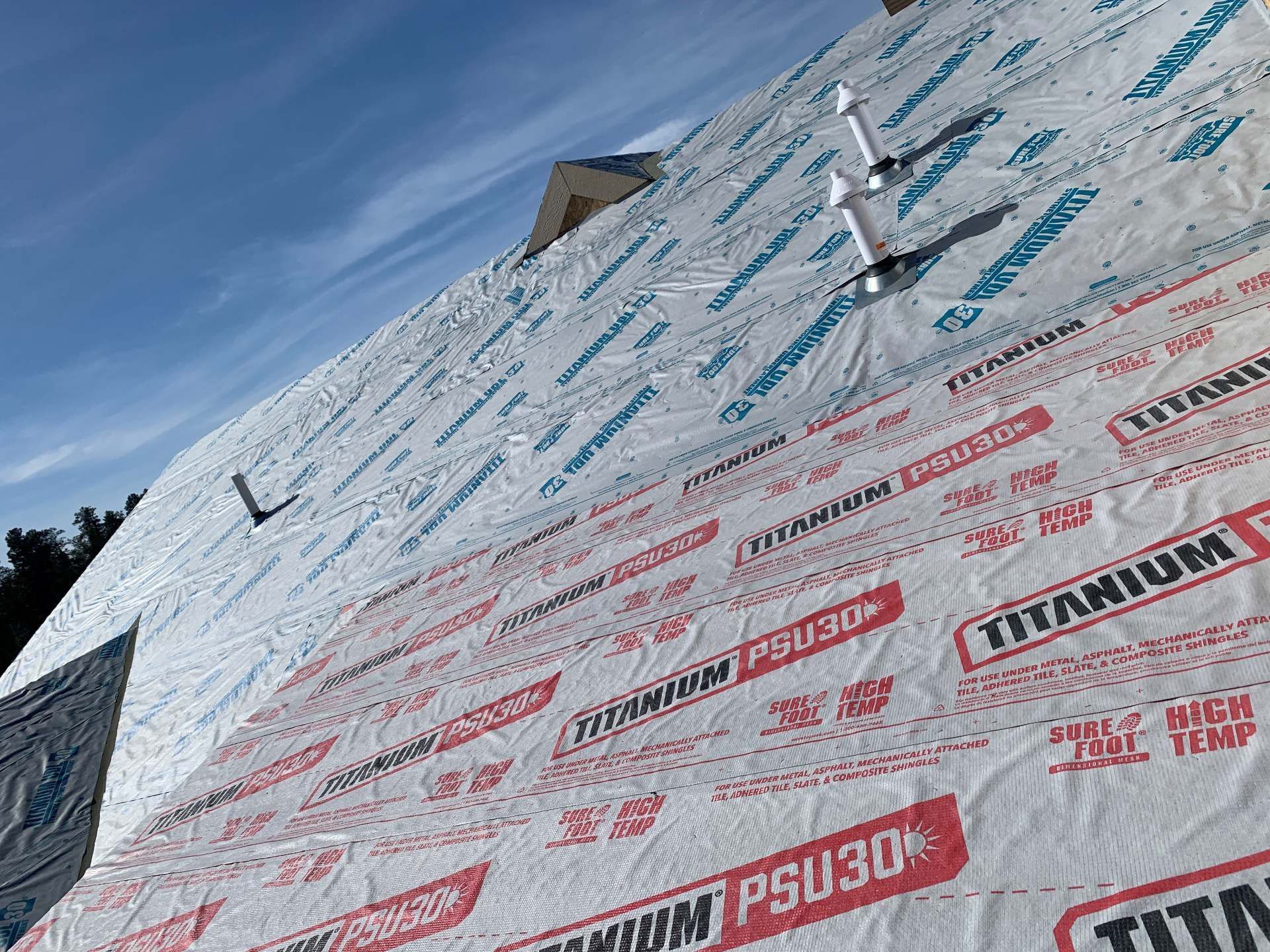 Partially wrapped roof with white weatherproofing under bright blue sky