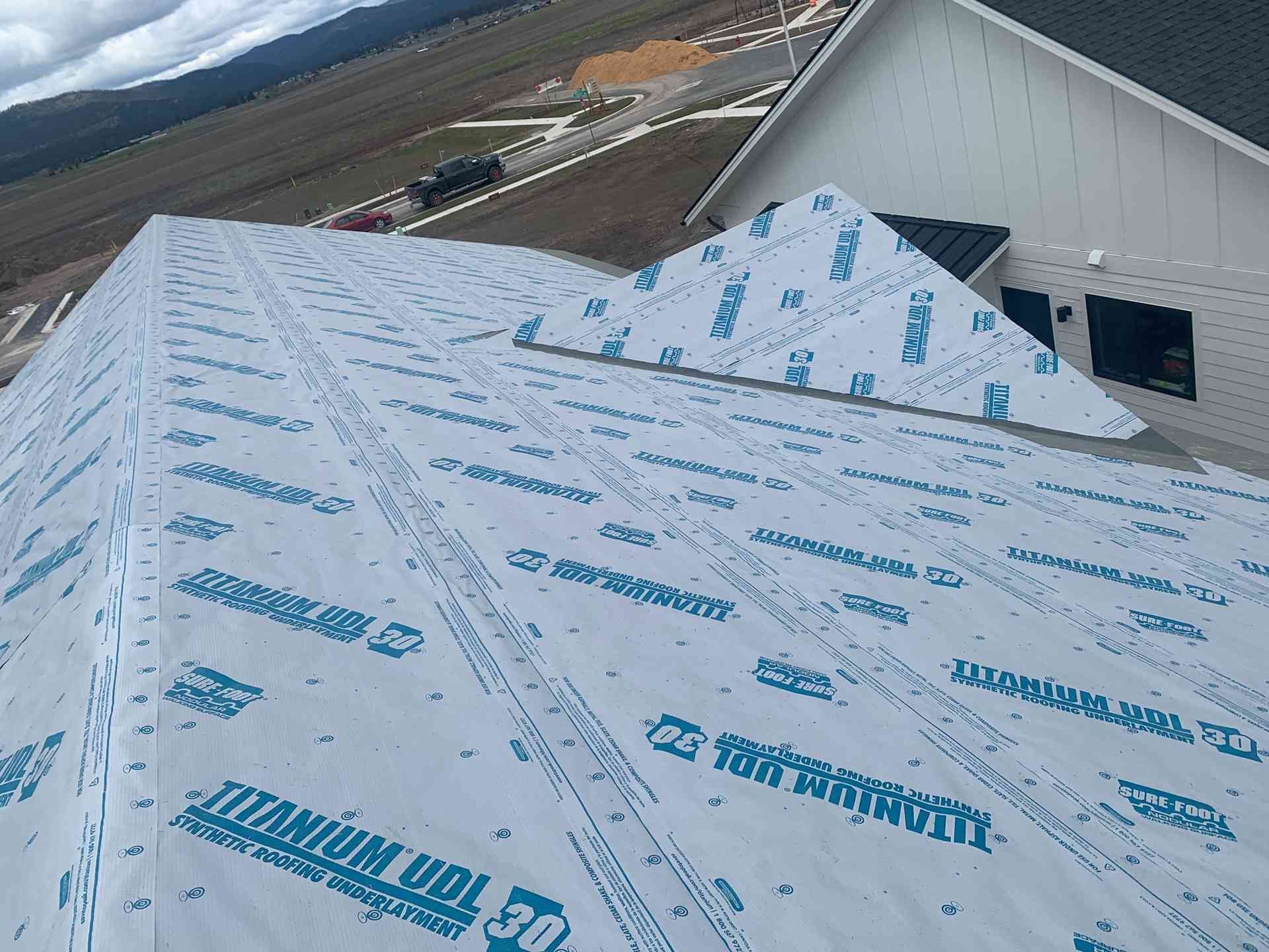Roof covered with blue-and-white underlayment beside a building on a sloped rooftop