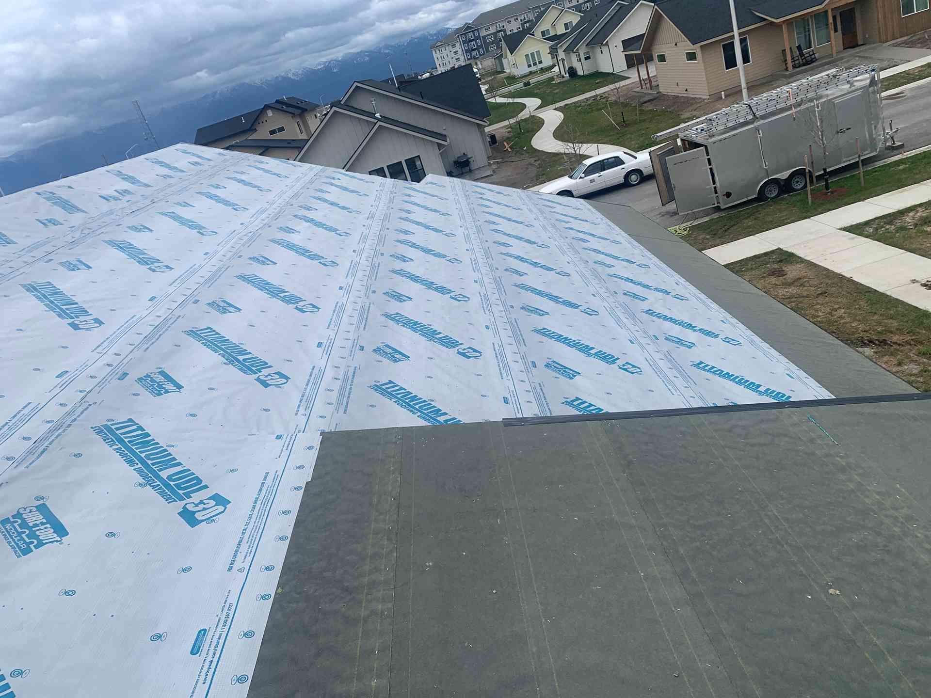 Roof under construction with white underlayment and gray shingles on a suburban house