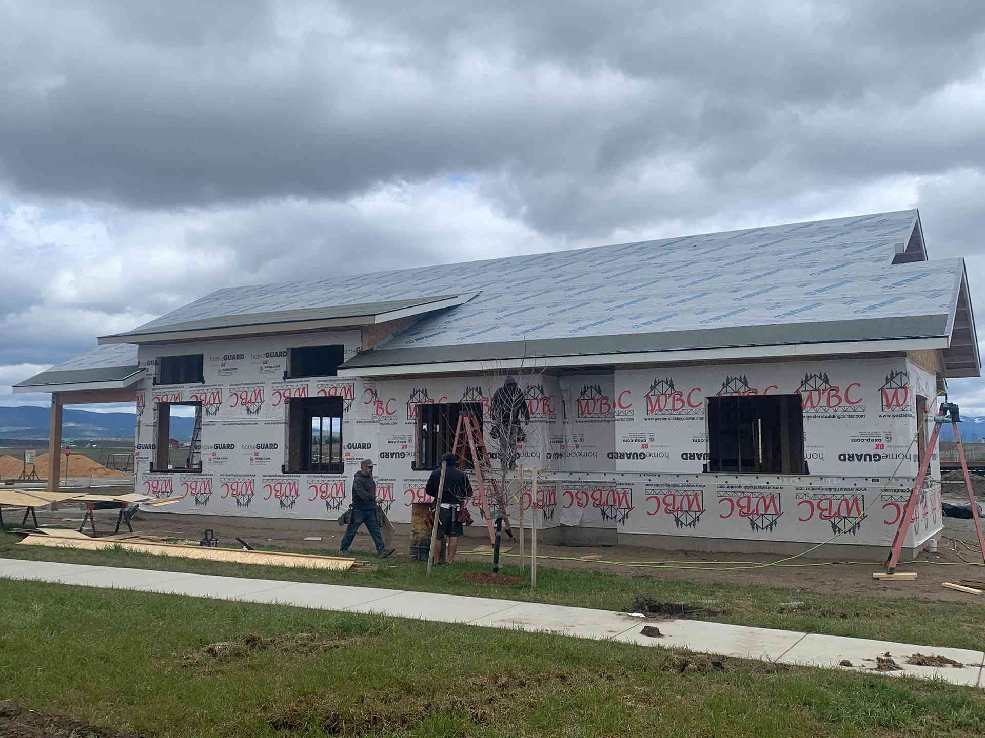 New house under construction with workers, gray roof, and cloudy sky