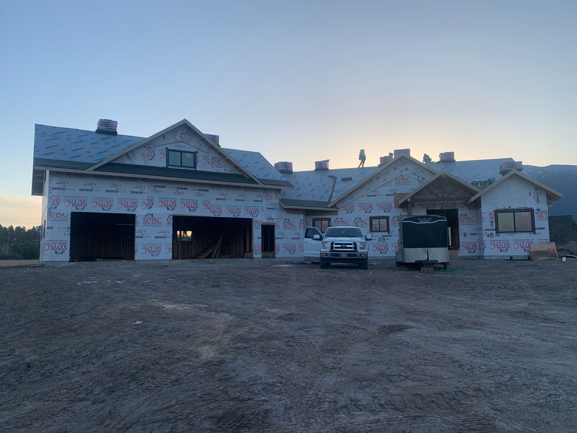 New house under construction with exposed framing, white wrap, and parked truck at dusk