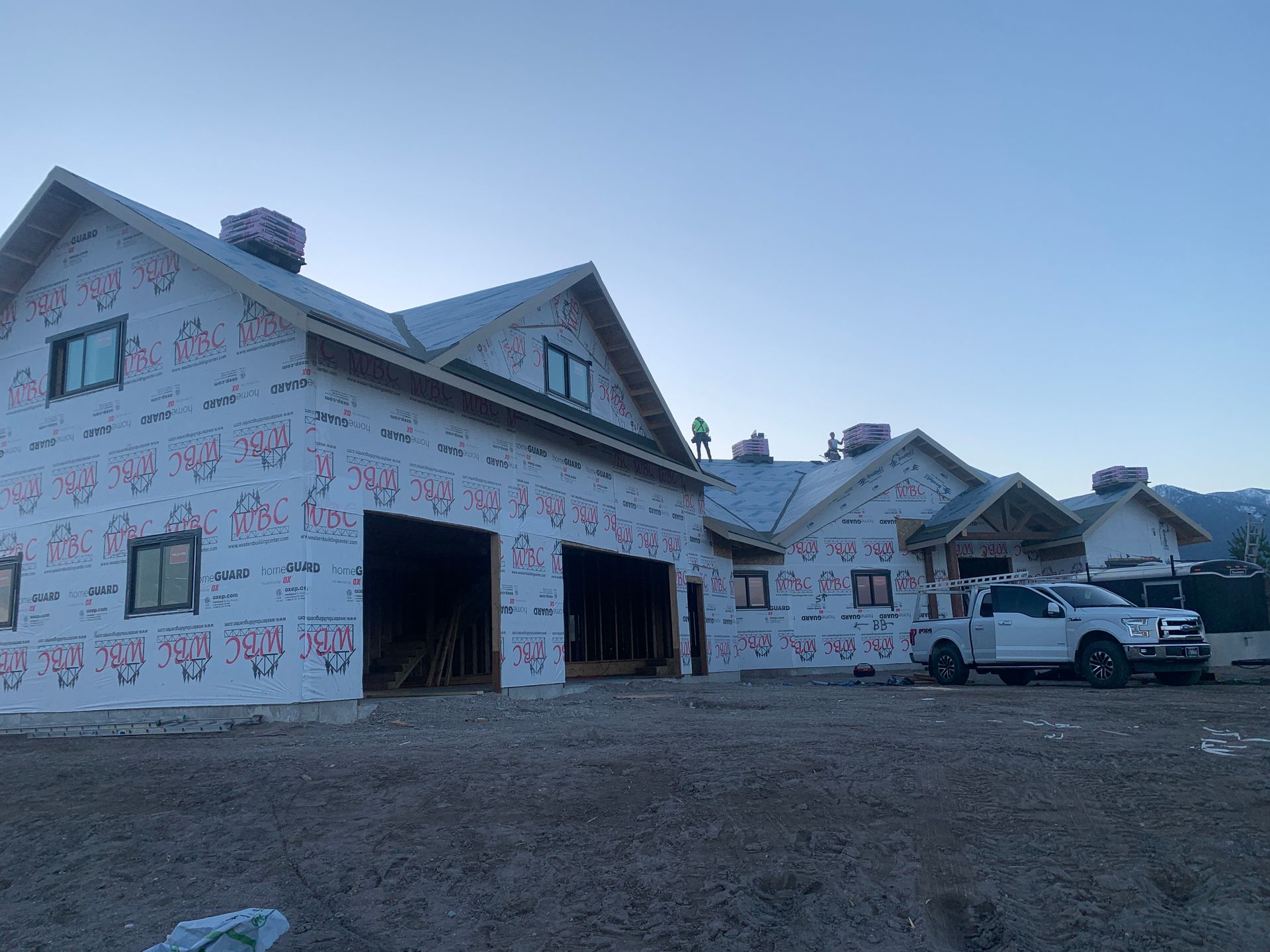 New homes under construction with white wrap, trucks parked outside, and a dirt lot at sunset